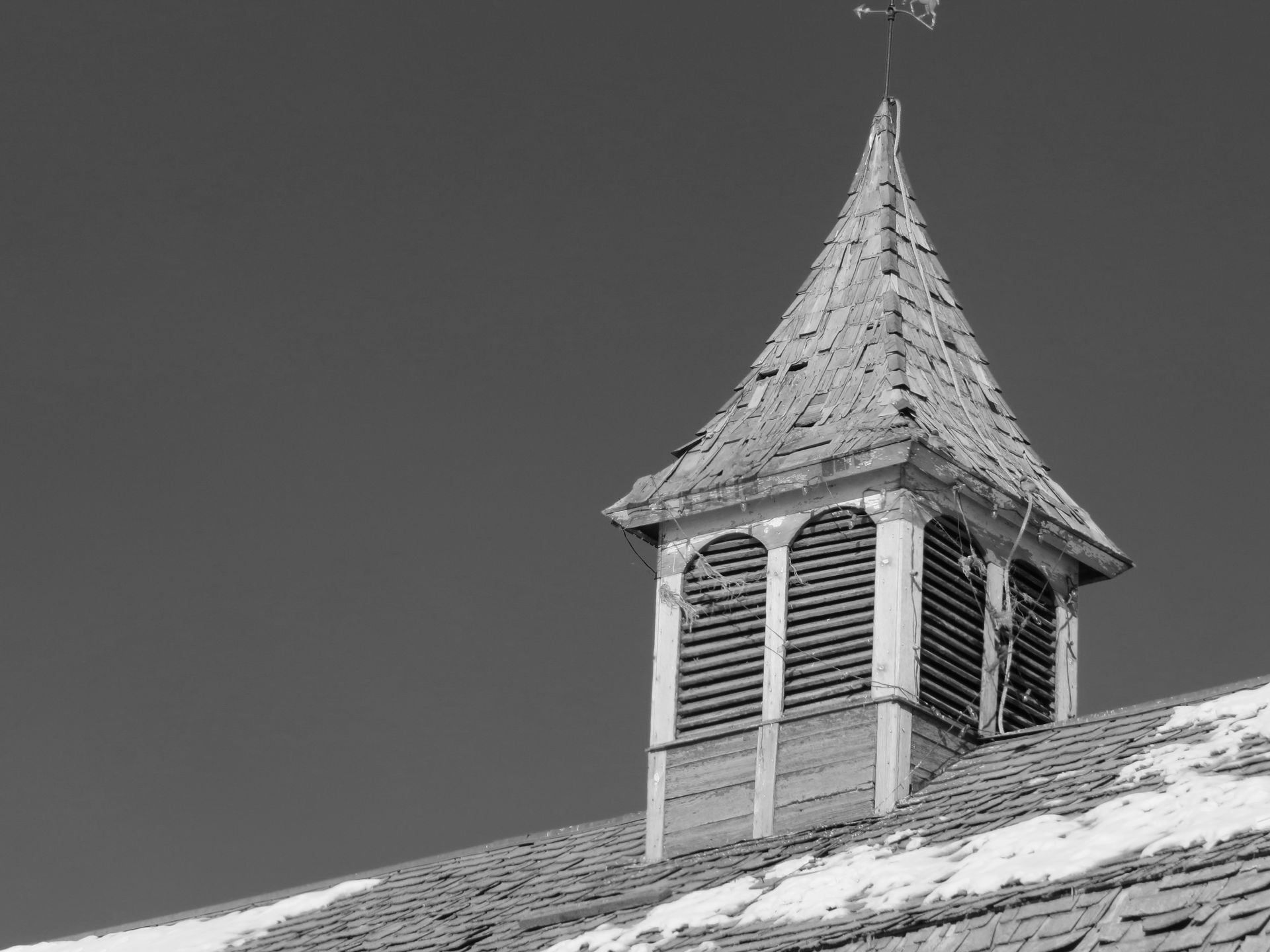 A black and white photo of a weather vane on top of a roof.