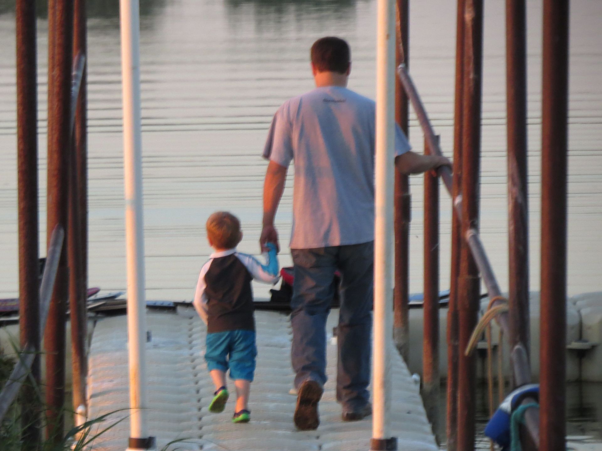 A man and child are walking on a dock holding hands