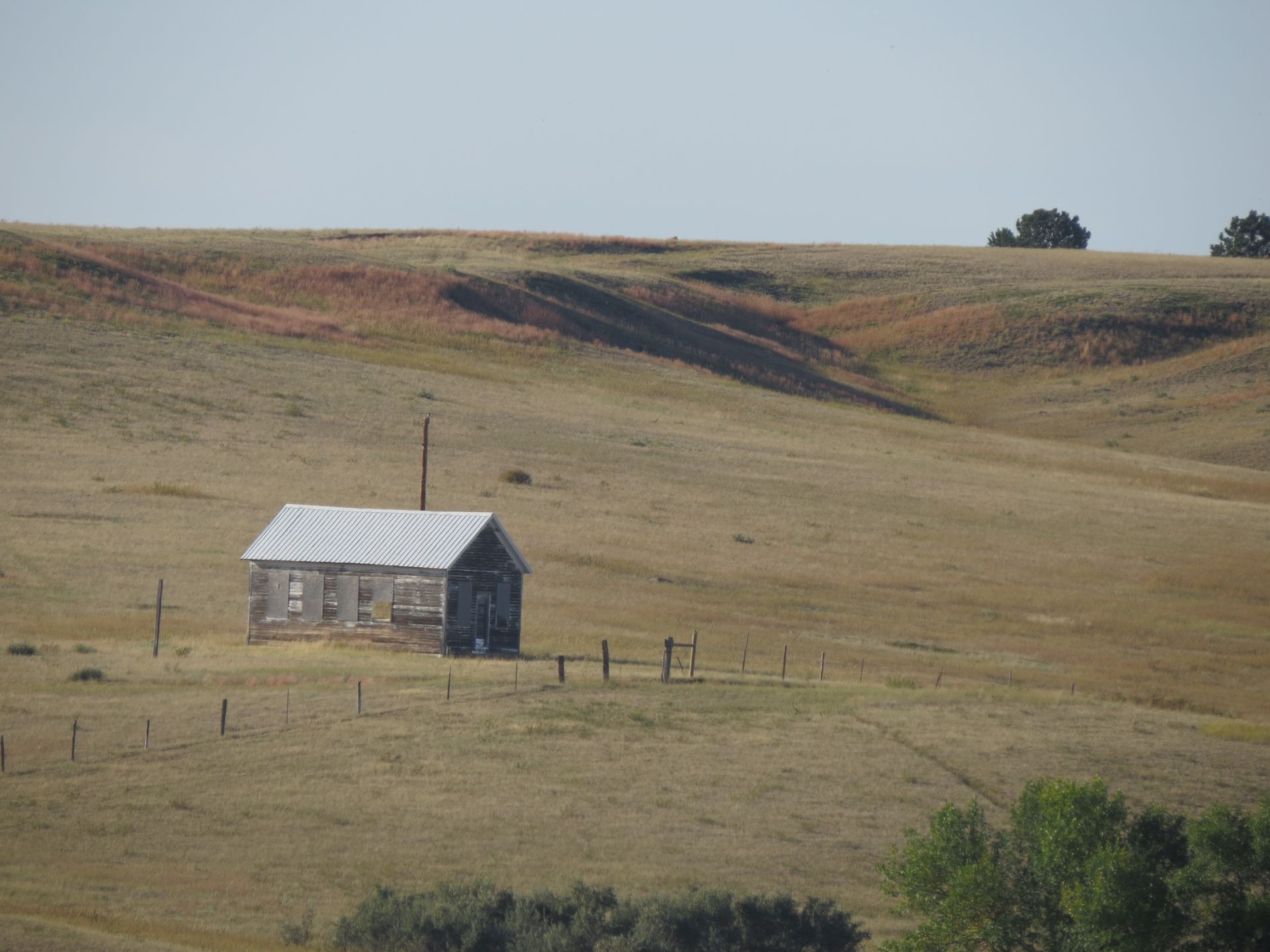 A small house is sitting in the middle of a dry grassy field.