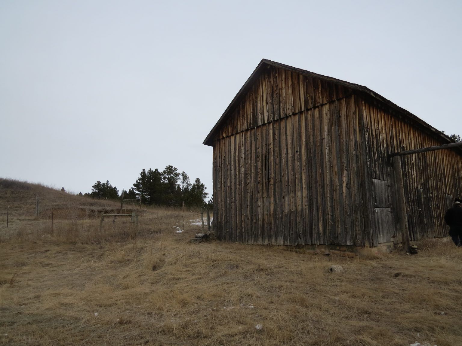 An old wooden barn is sitting in the middle of a dry grass field.