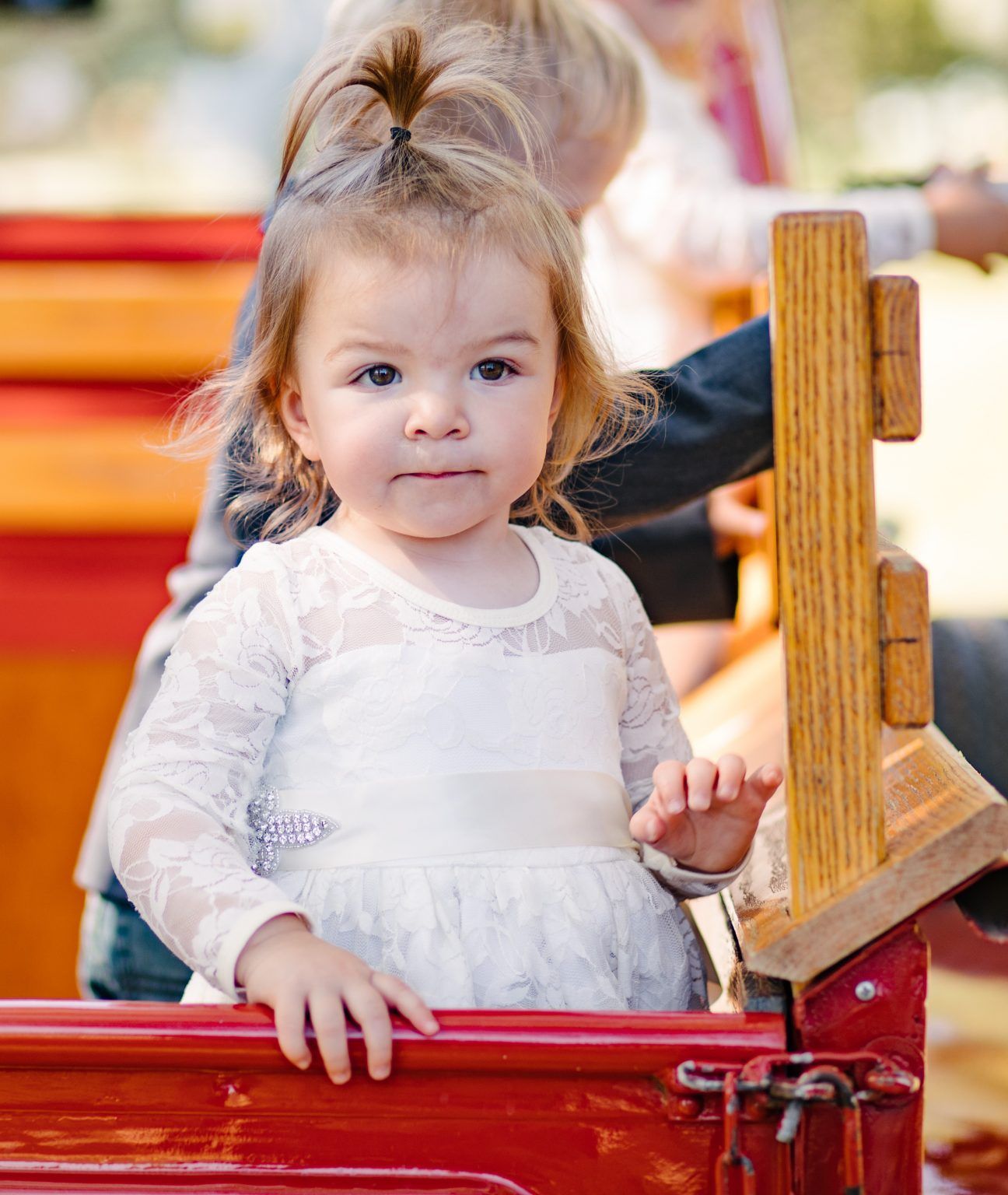 A little girl in a white dress is sitting in the back of a red truck.