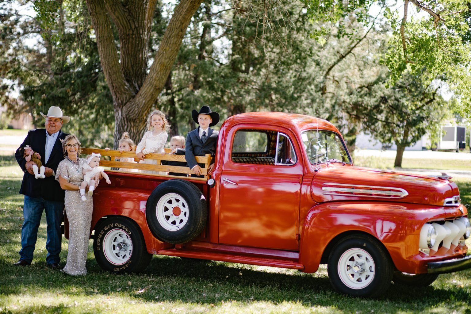 A family is posing for a picture in front of an old red truck.