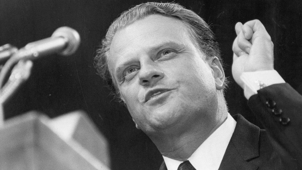 A man in a suit and tie is speaking into a microphone.