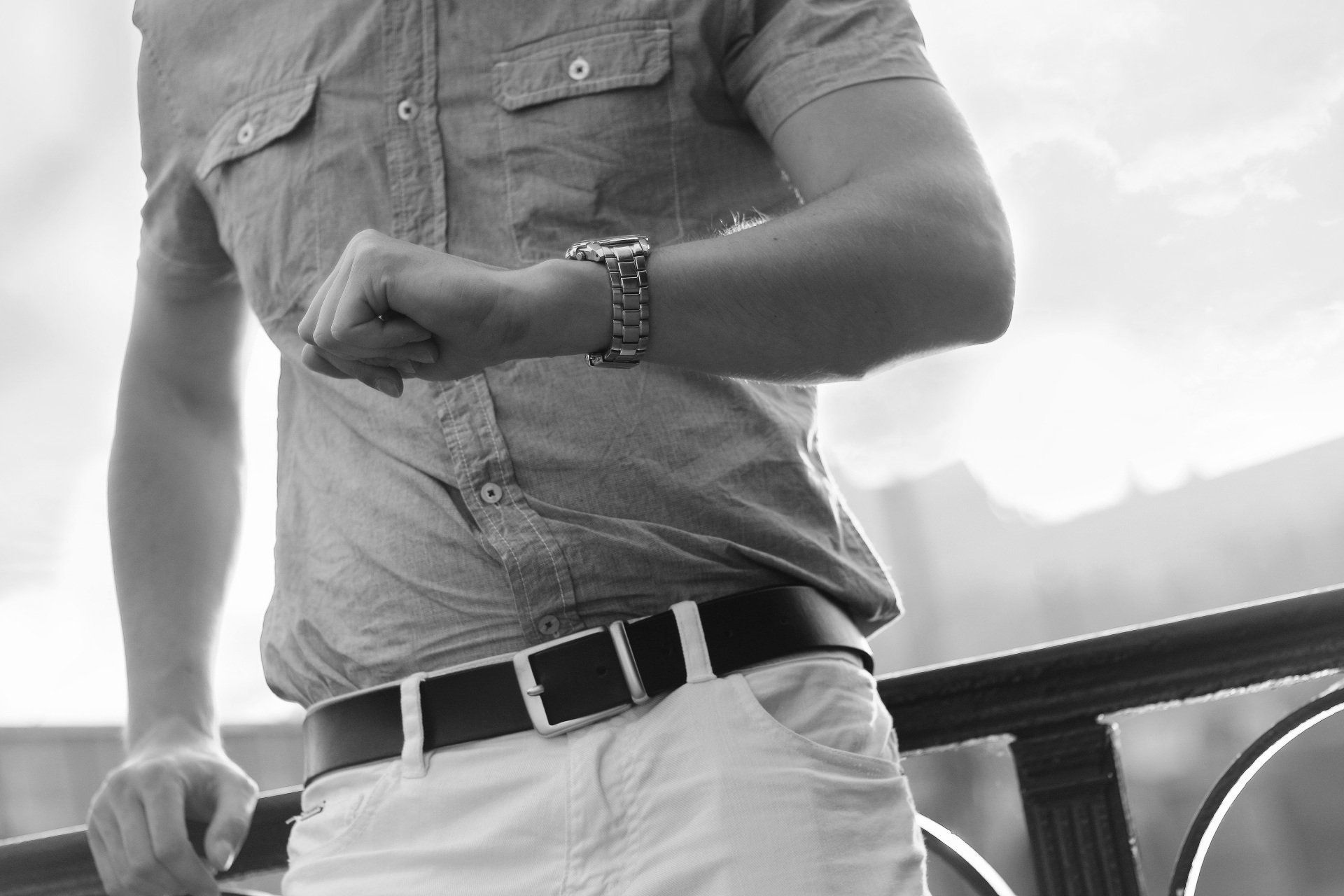 A man is standing on a railing looking at his watch.