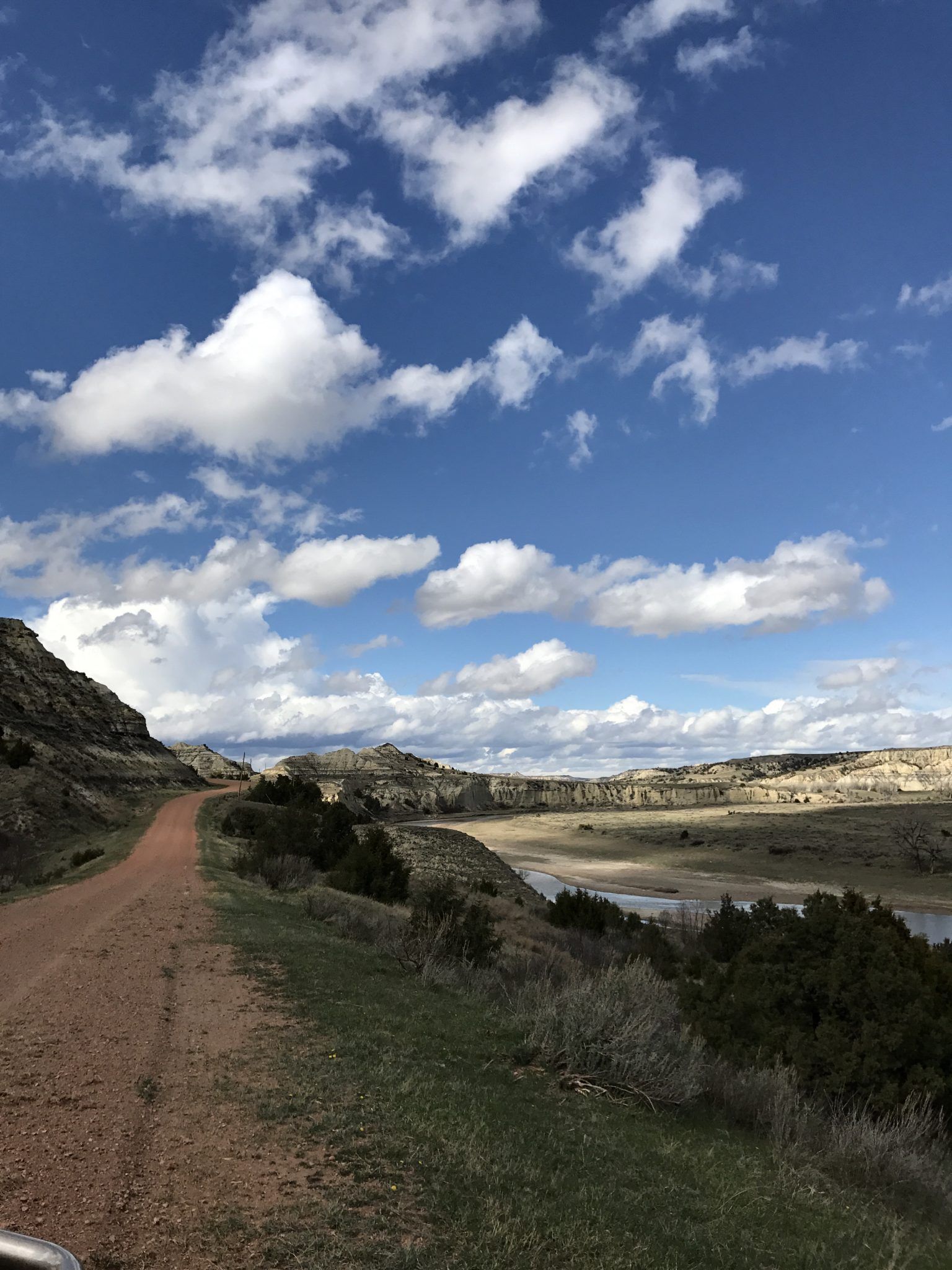 A dirt road leading to a lake with a blue sky and clouds.