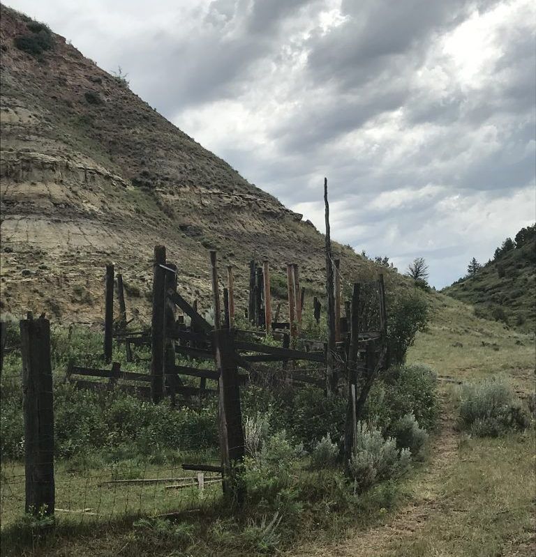 A wooden fence surrounds a grassy hillside on a cloudy day