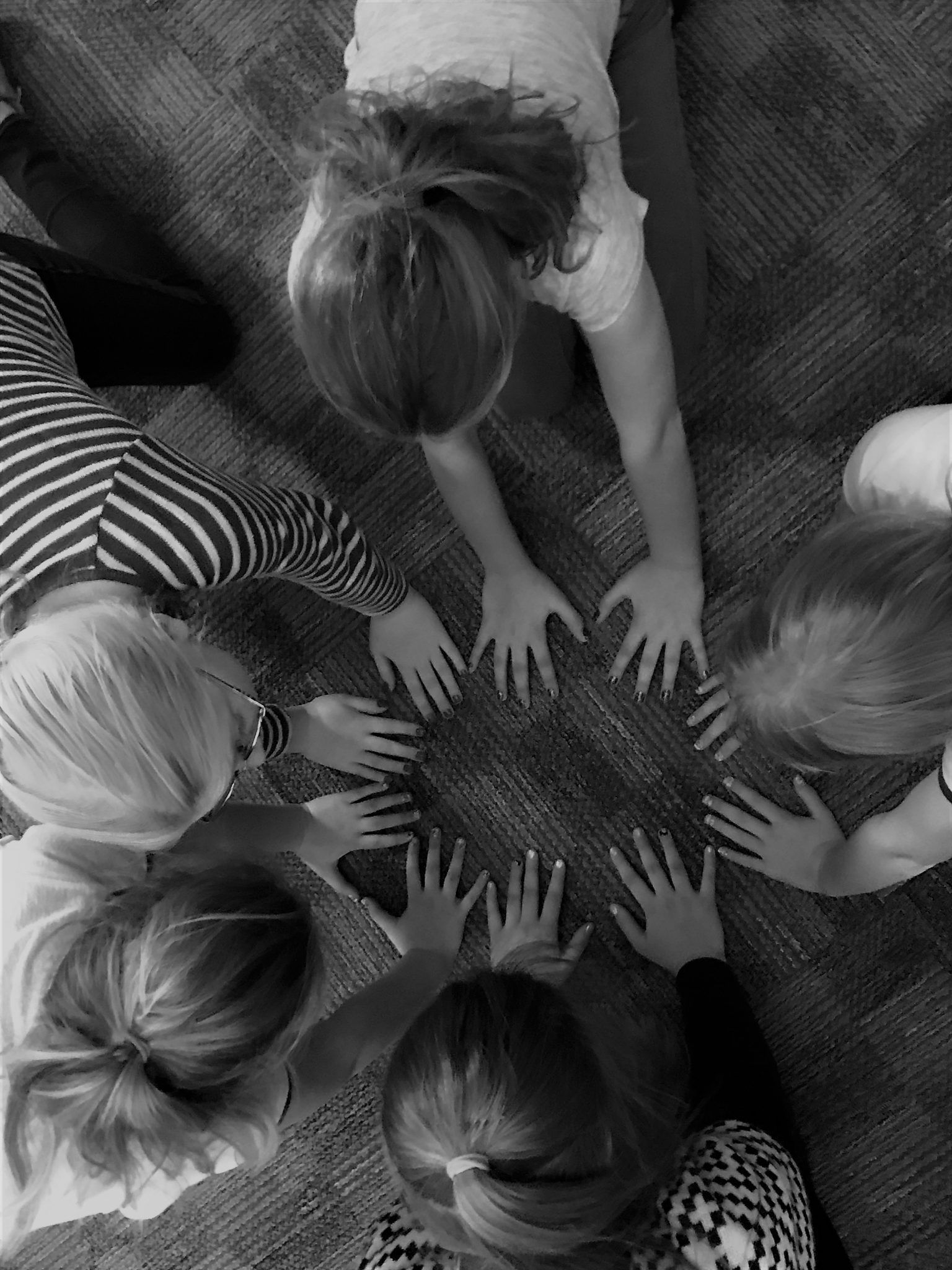 A group of children are laying on the floor in a circle with their hands in the middle.