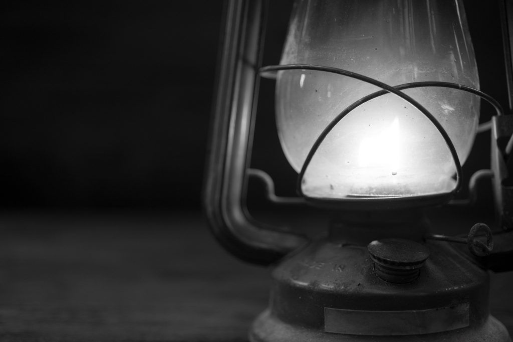 A black and white photo of an old lantern with a light inside of it.