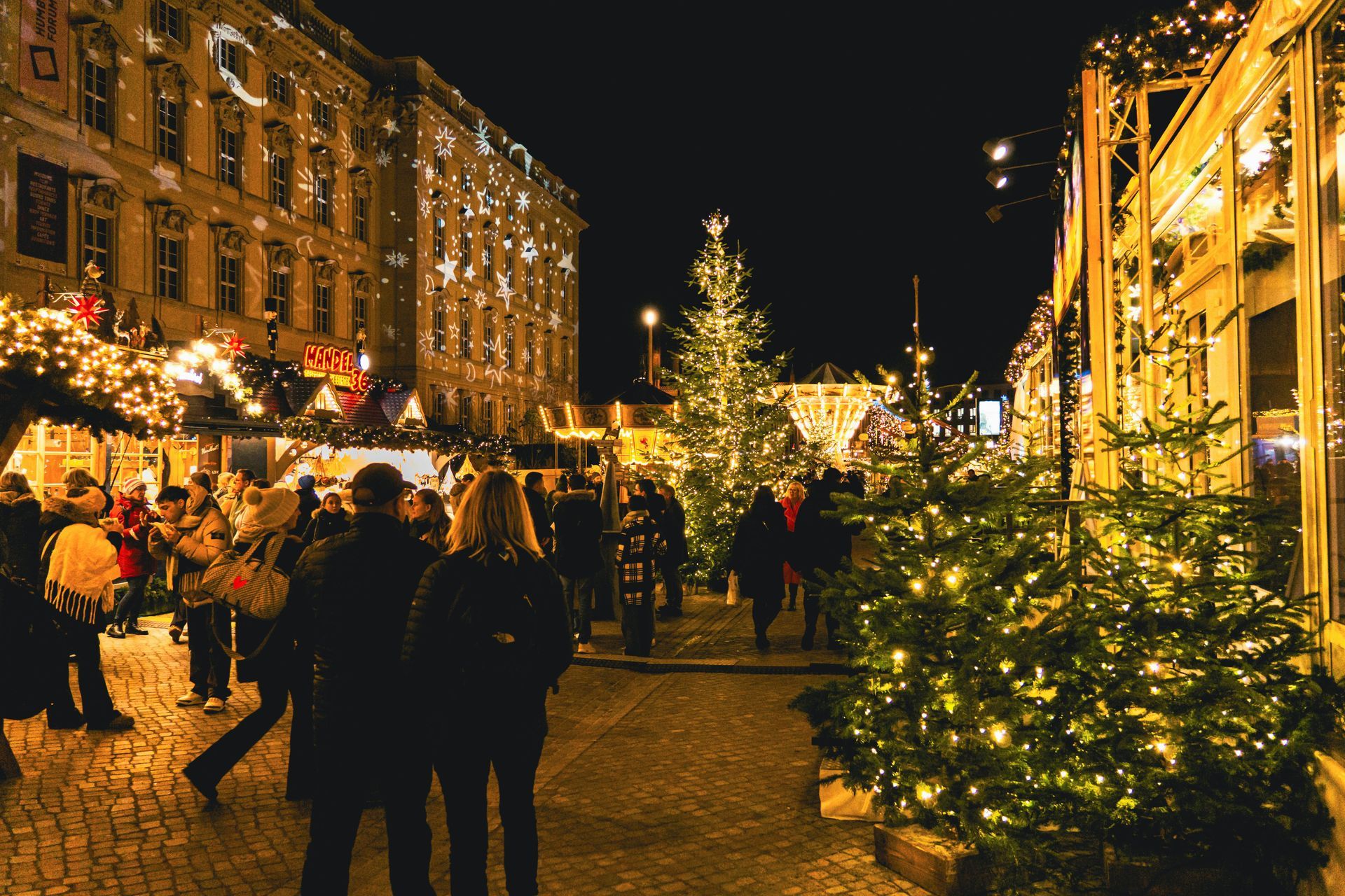 A group of people are walking down a cobblestone street at a christmas market.
