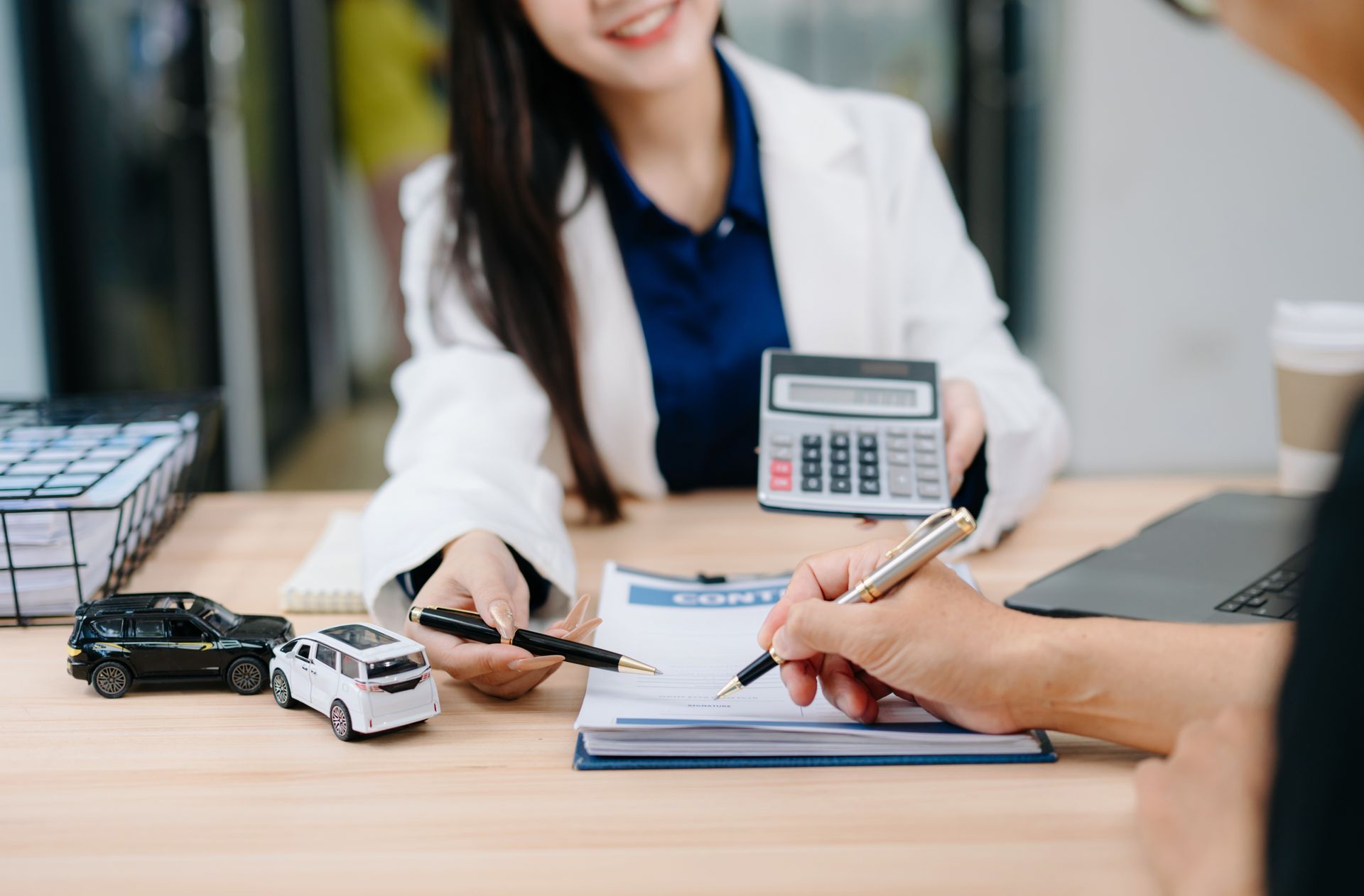 Agent calculates costs while client signs auto insurance policy paperwork at desk