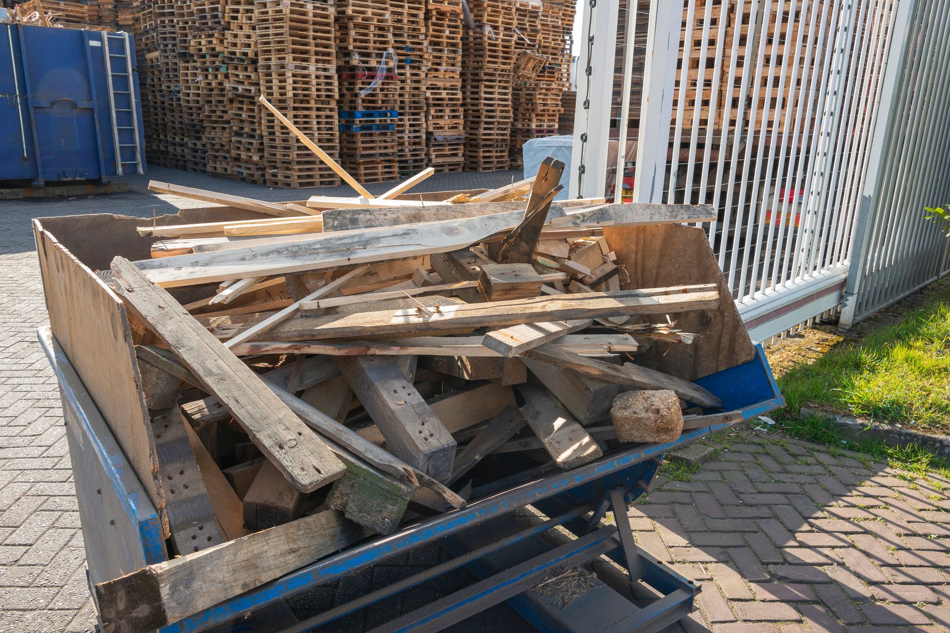 A wheelbarrow filled with wood is parked in front of a pile of wooden pallets.