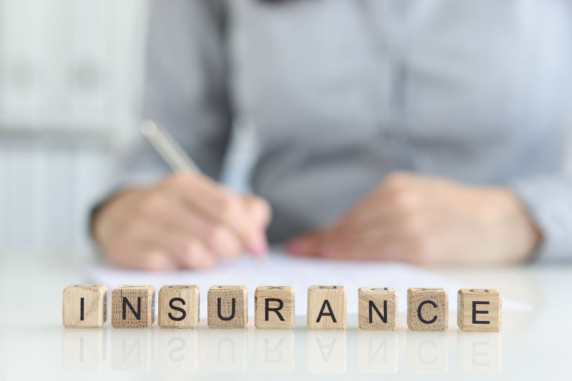Business insurance agency concept with wooden blocks spelling INSURANCE and person signing document.