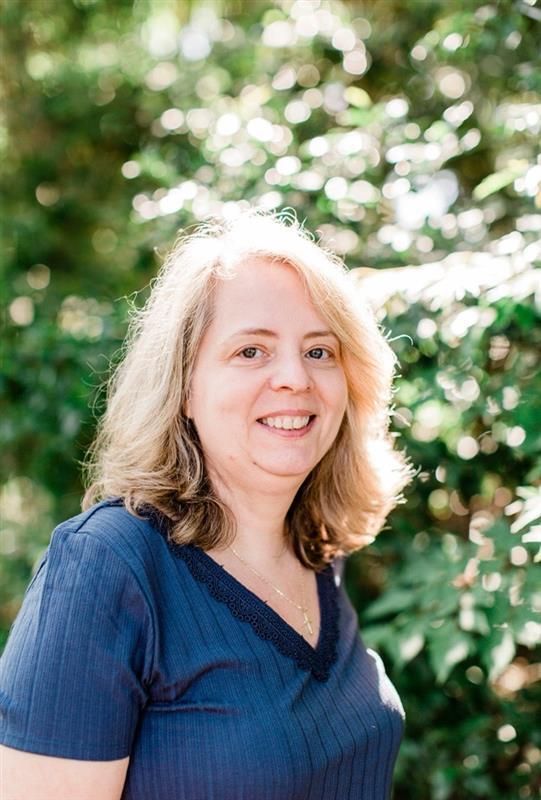 A woman in a paisley shirt is standing in front of a plant.