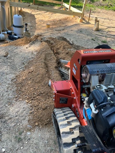 A red tractor is cutting a hole in the ground.