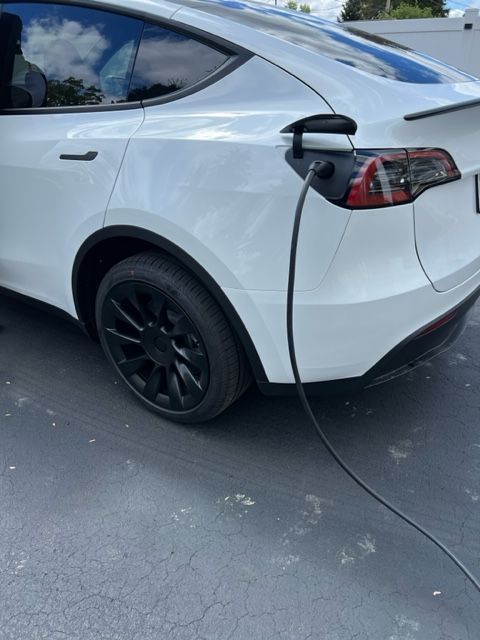 A white tesla model y is being charged at a charging station