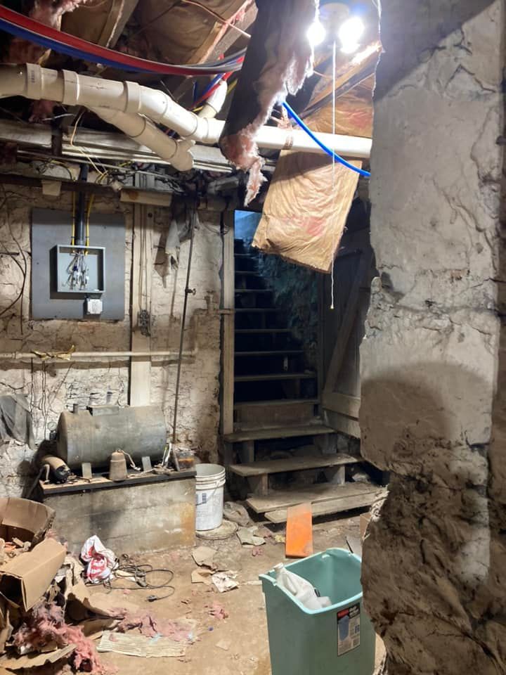 A dirty basement with stairs and a trash can.