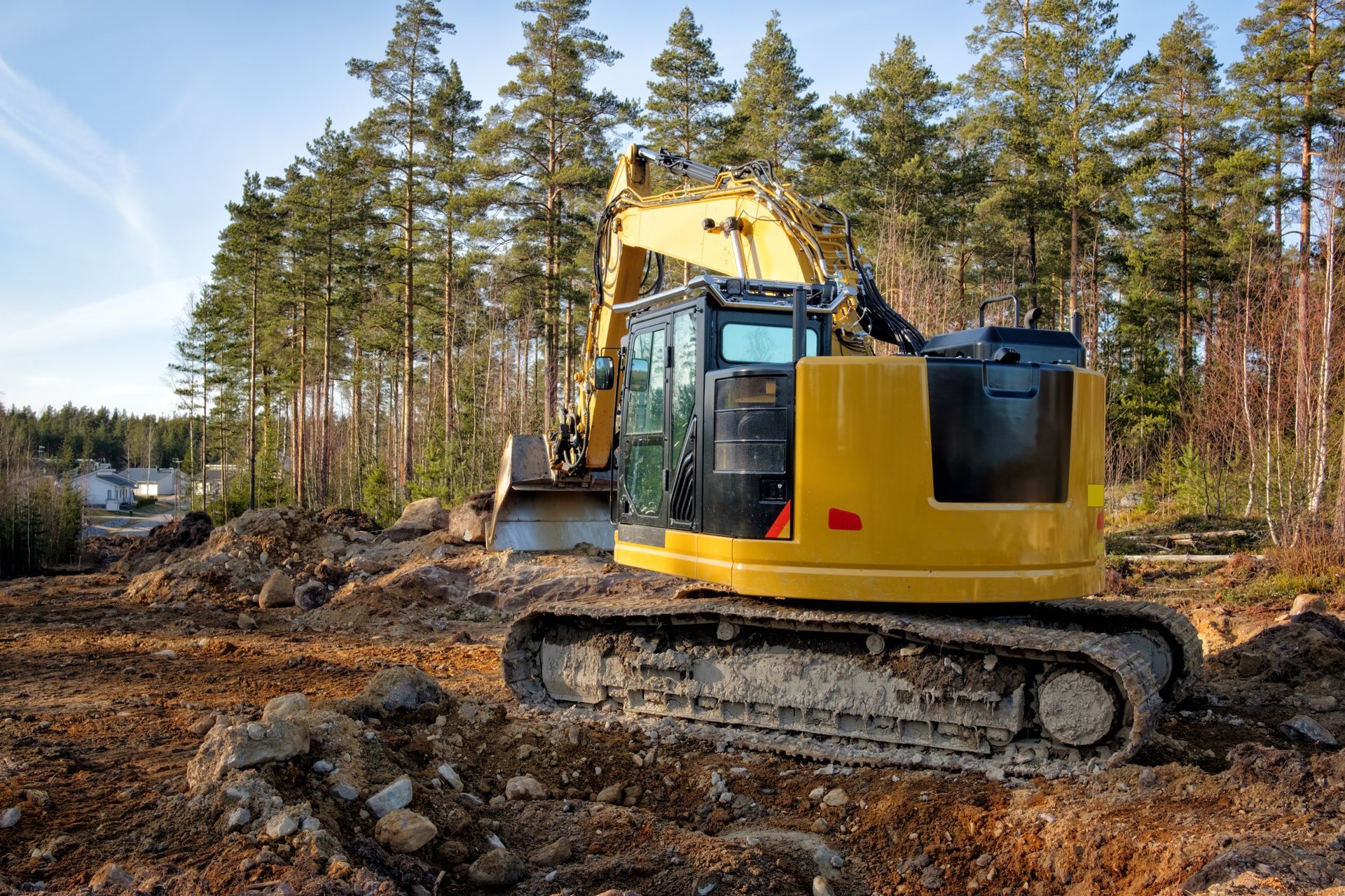 Une pelleteuse jaune sur un terrain boueux, en train de défricher une forêt, avec des arbres et un ciel bleu en arrière-plan.