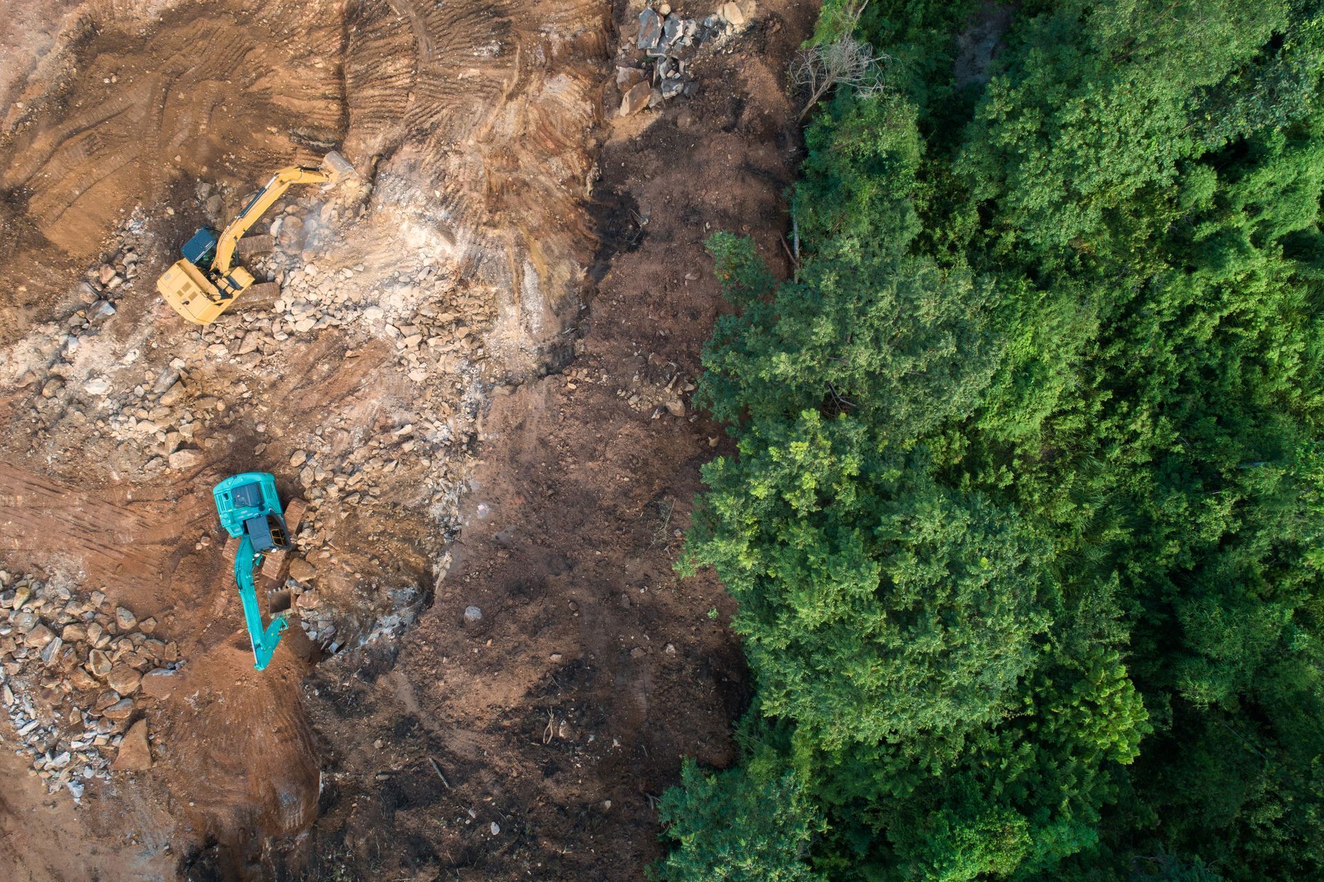 Vue aérienne : Des excavatrices déblayent un terrain à proximité d'une forêt verdoyante.