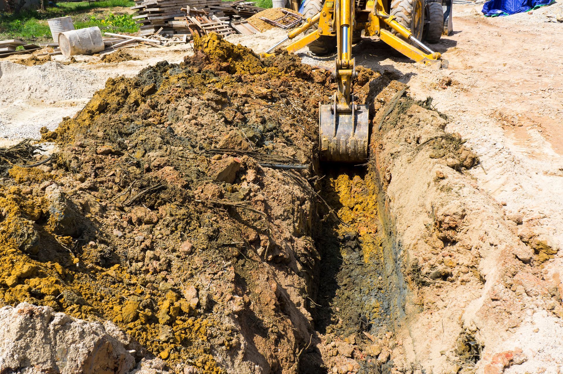 Une pelleteuse creuse une tranchée dans la terre, créant un tas de terre brune et jaune.