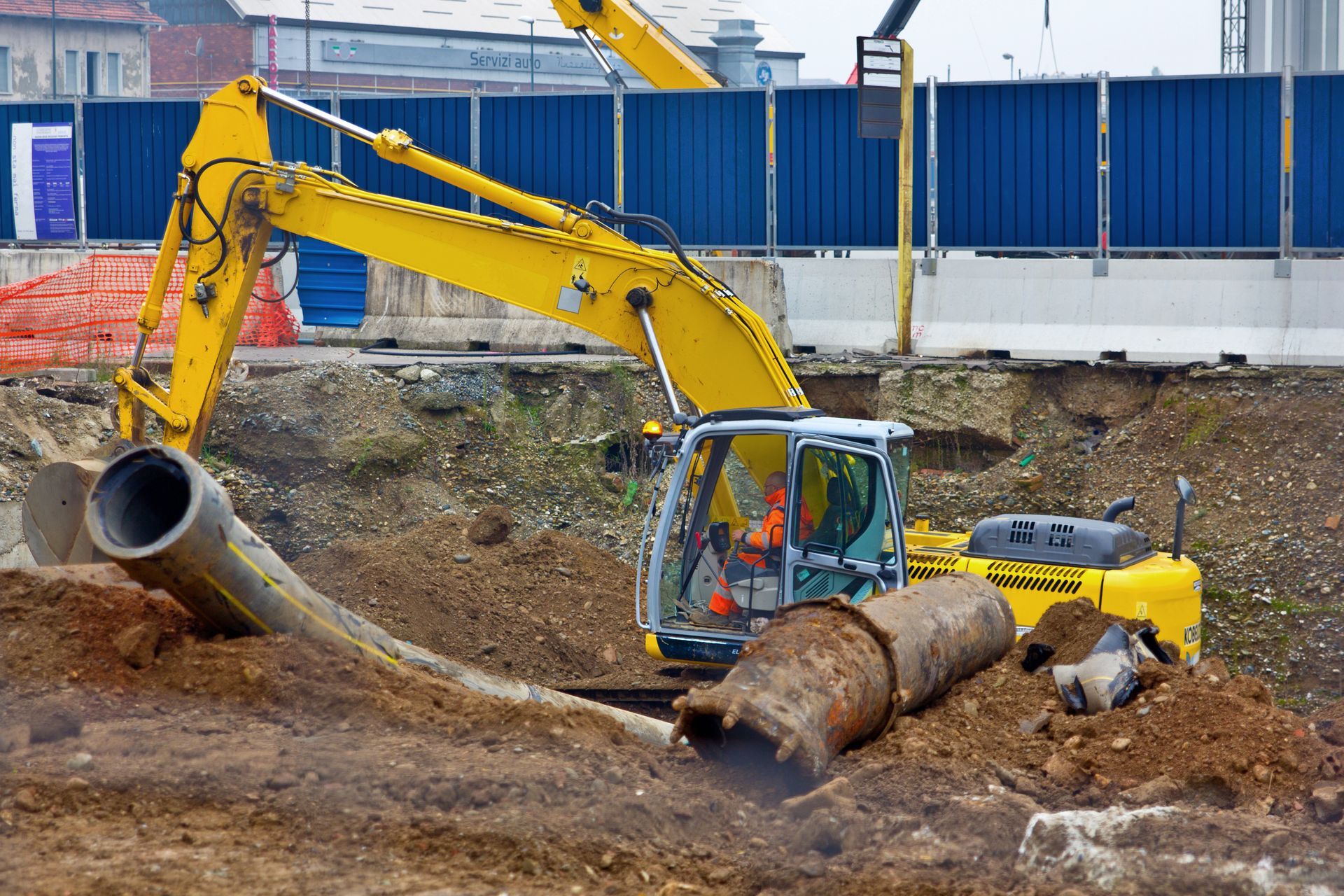 Une pelleteuse jaune creuse sur un chantier de construction, parmi des tuyaux et de la terre.