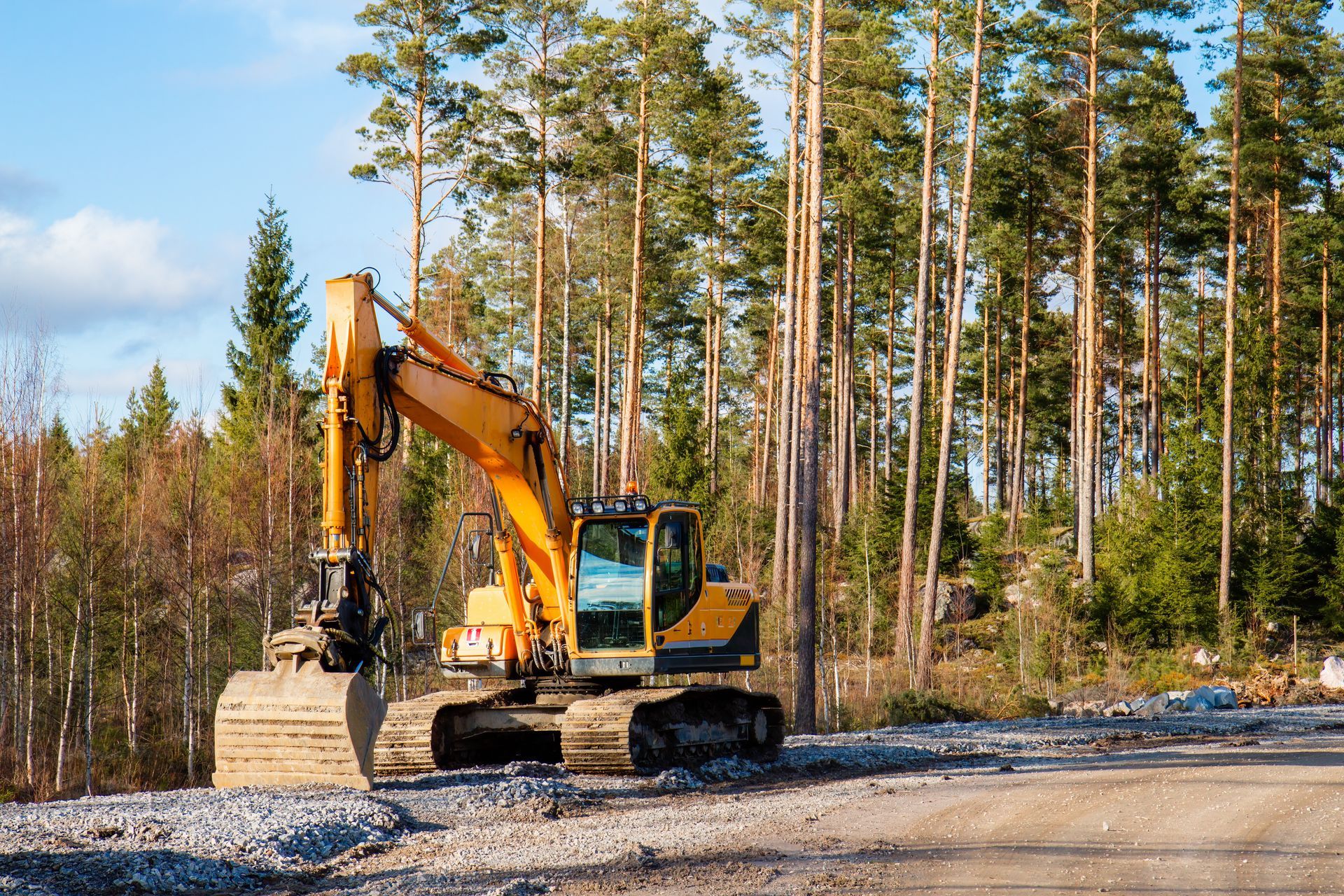 Une pelleteuse jaune sur un chemin de terre, défrichant une forêt par une journée ensoleillée.