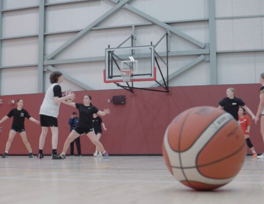 Basketball practice in a gym, with players near the hoop and a large basketball in the foreground