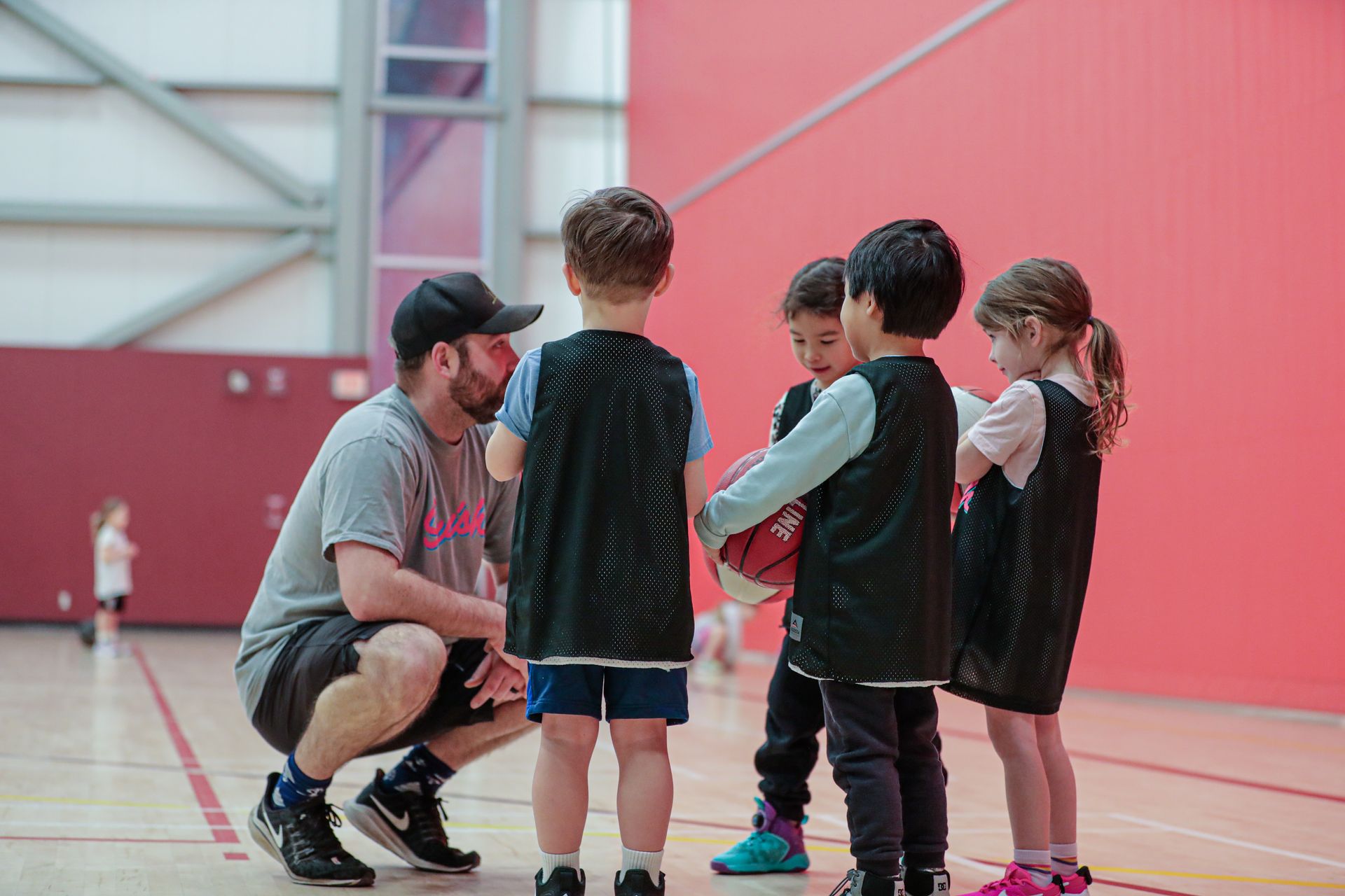 Coach kneeling with four children in a gym, talking in a huddle during sports practice