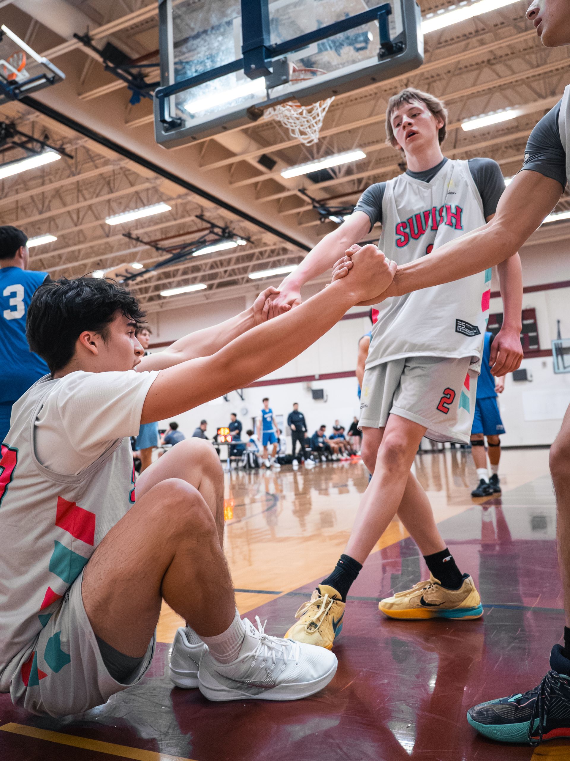 Basketball players in gray uniforms helping each other up on a gym court during a game