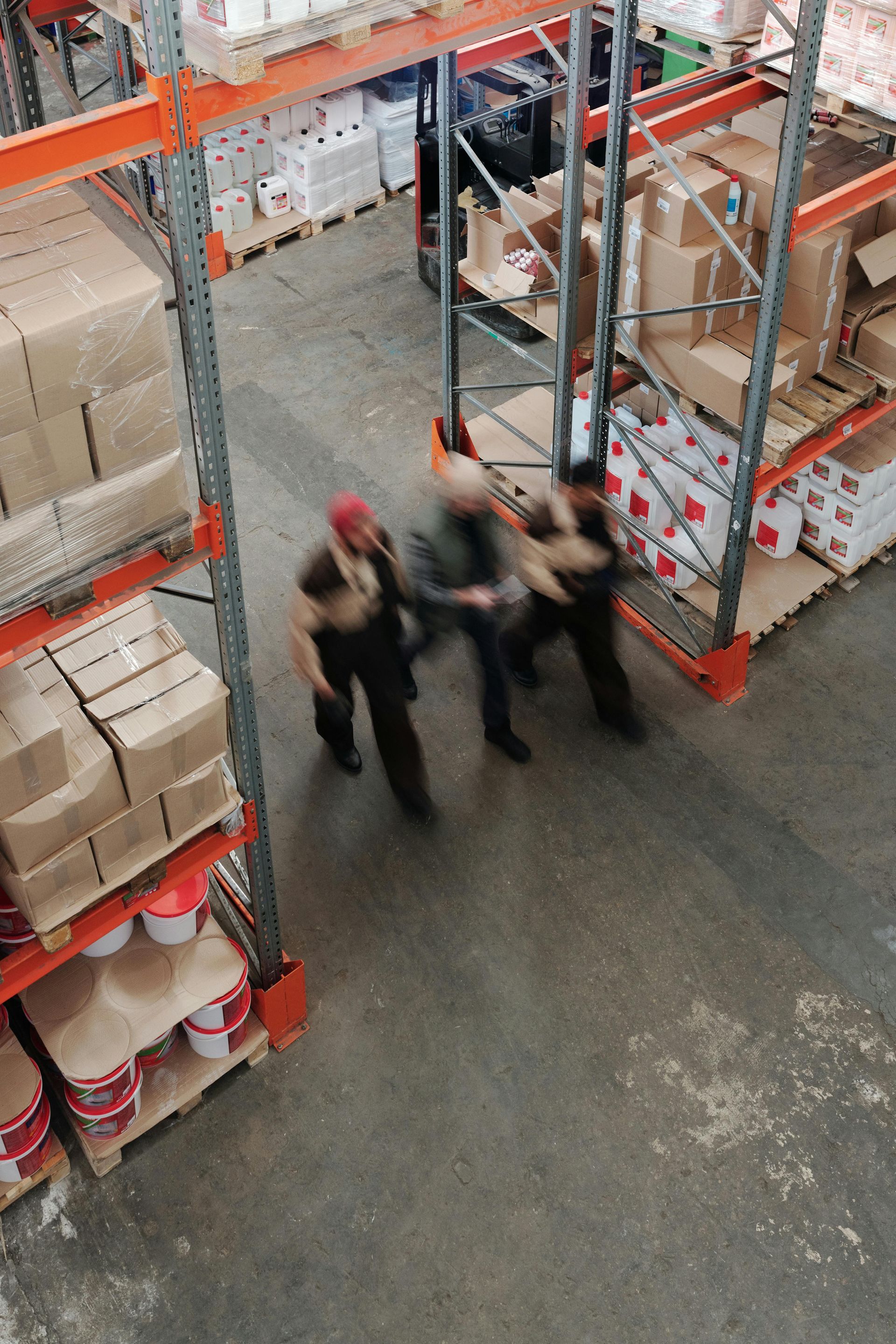 Workers moving through a warehouse. Boxes and materials on shelves, with motion blur indicating movement.