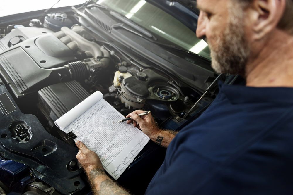 Mechanic Inspecting Car Engine, Writing on Notepad; Garage Setting — Nova Auto Innovations in Charlestown, NSW