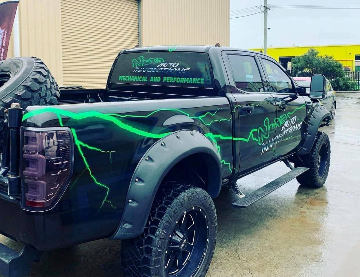 Black truck with green lightning design, off-road tires, and flares, parked outside.