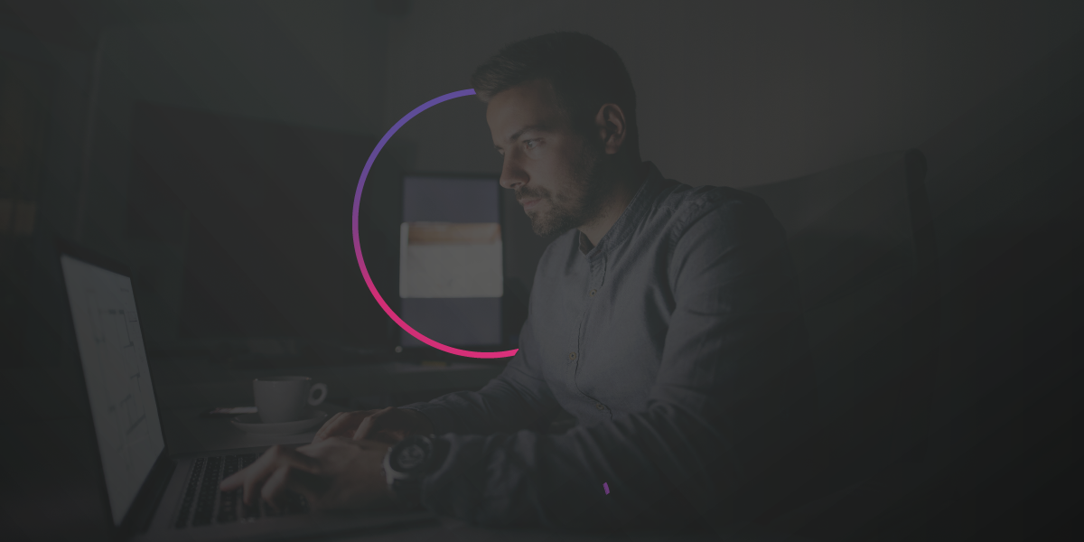 Um homem está sentado em frente a um computador em um quarto escuro.