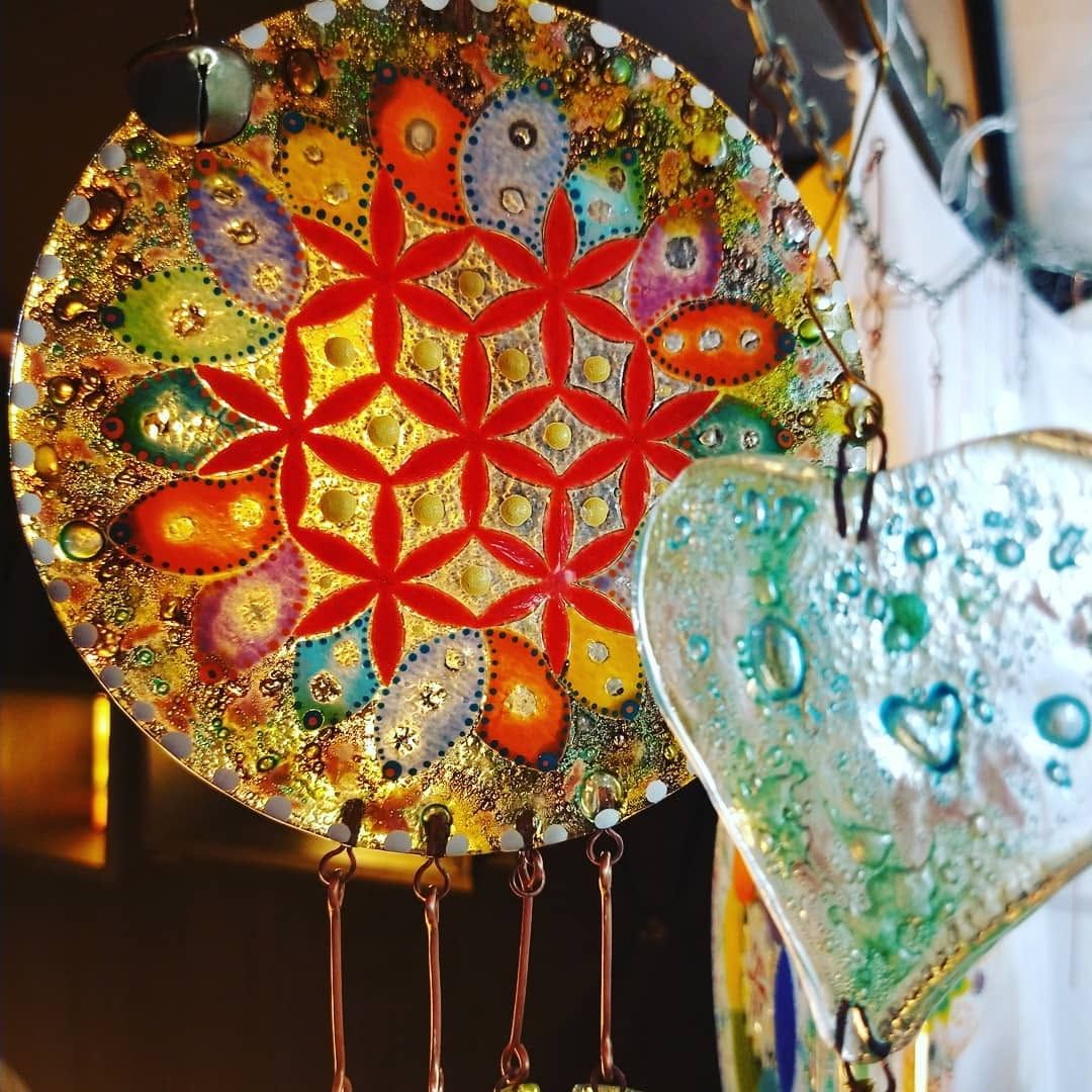 Colorida campanilla de viento con mosaico, centro floral rojo y corazón de cristal azul sobre fondo difuminado.
