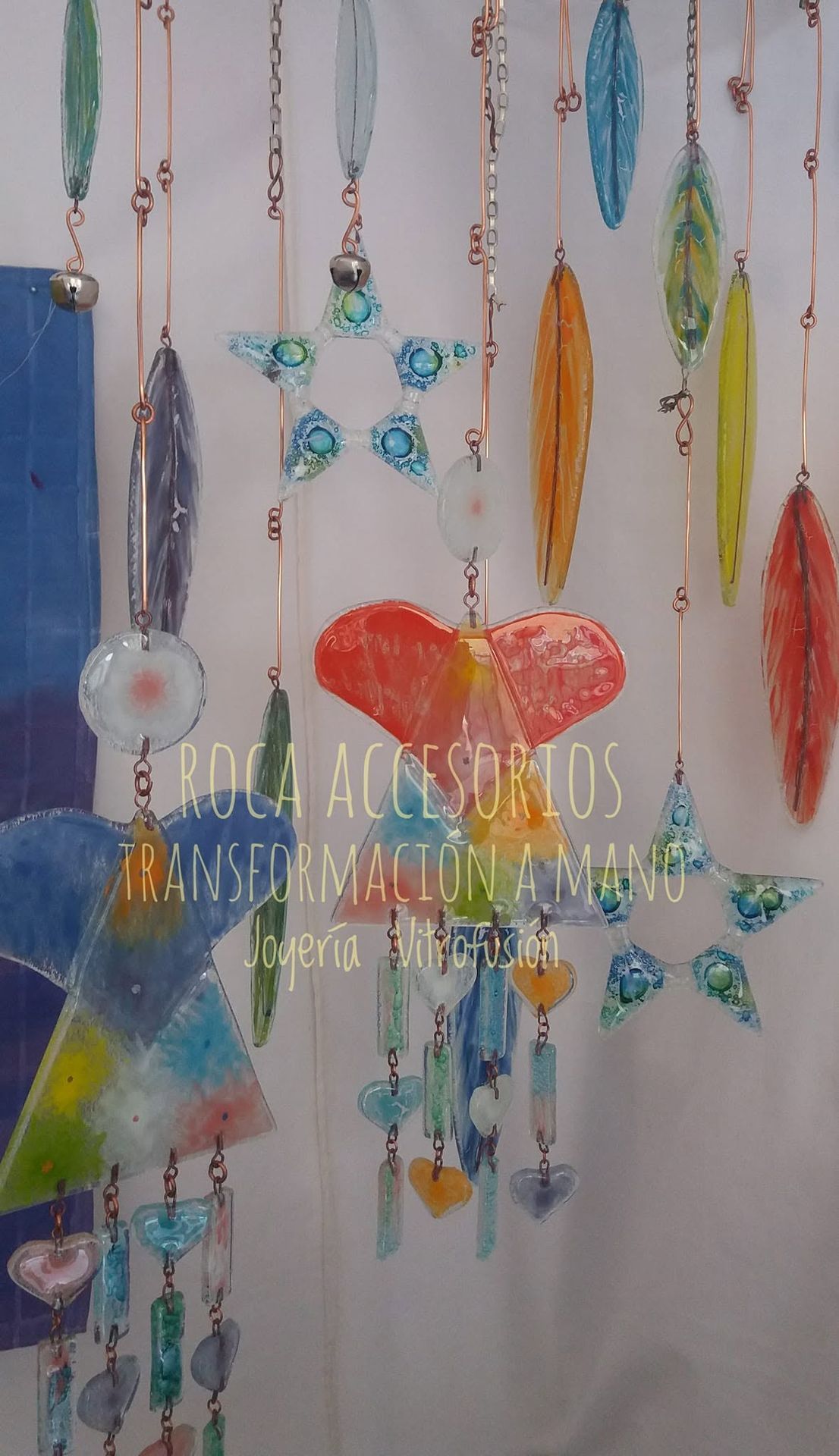Adornos de cristal colgantes y flores de colores expuestos sobre una pared clara con texto manuscrito en el centro.