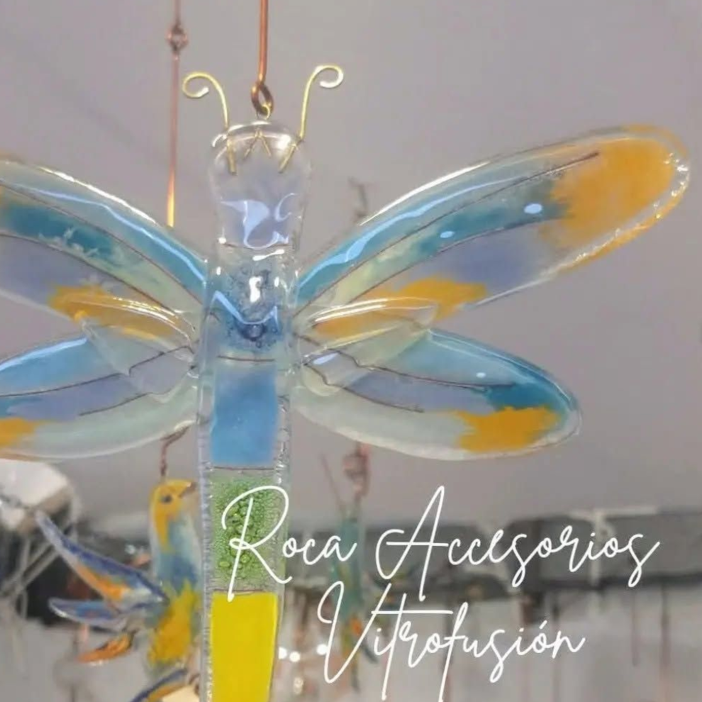 Libélula de cristal azul y amarillo con alas transparentes y detalles dorados, con el texto “Roca Accesorios Vitrofusión”.