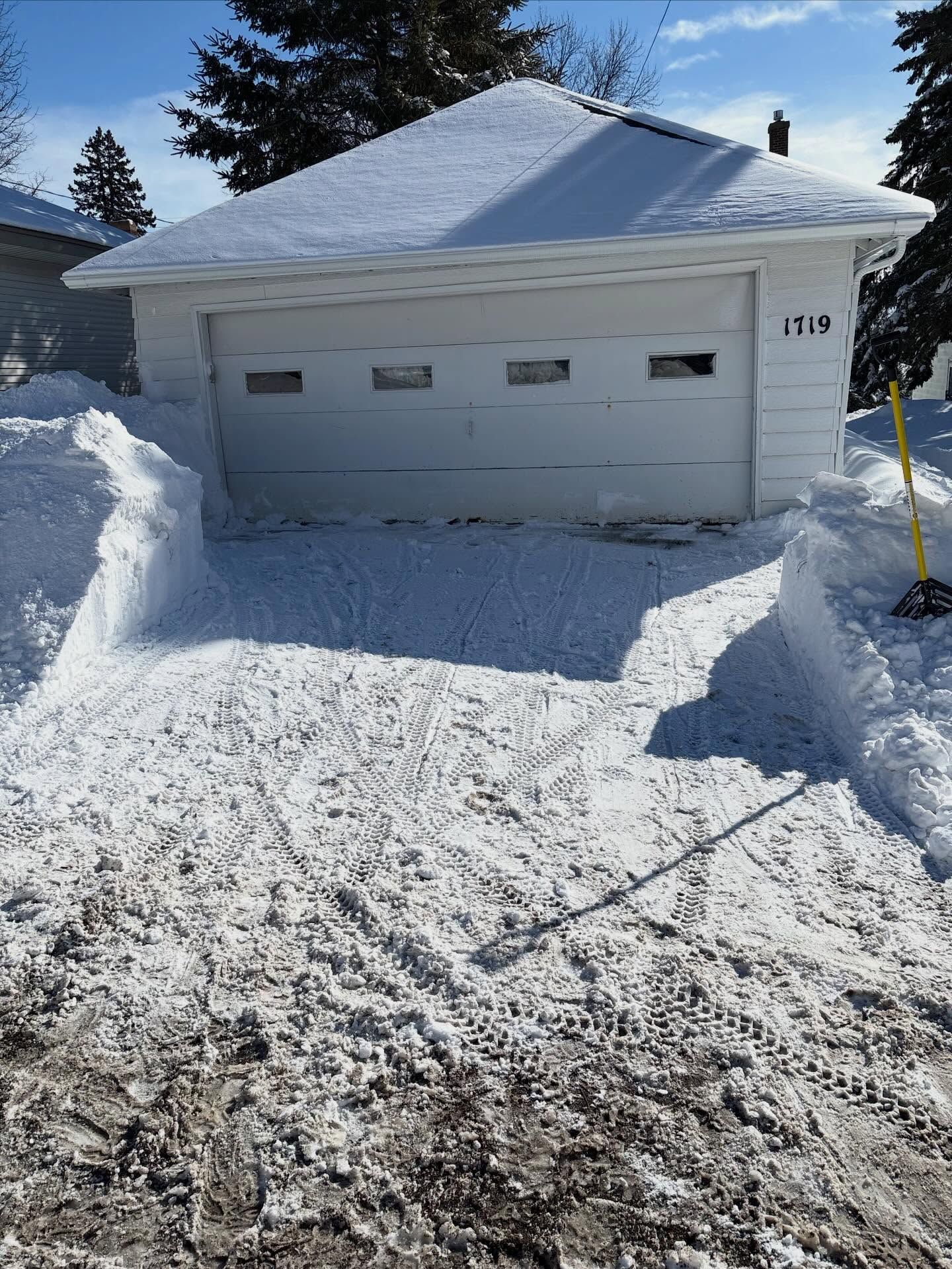 Snow-covered suburban garage and driveway after heavy snowfall, with a small house number visible on the side.