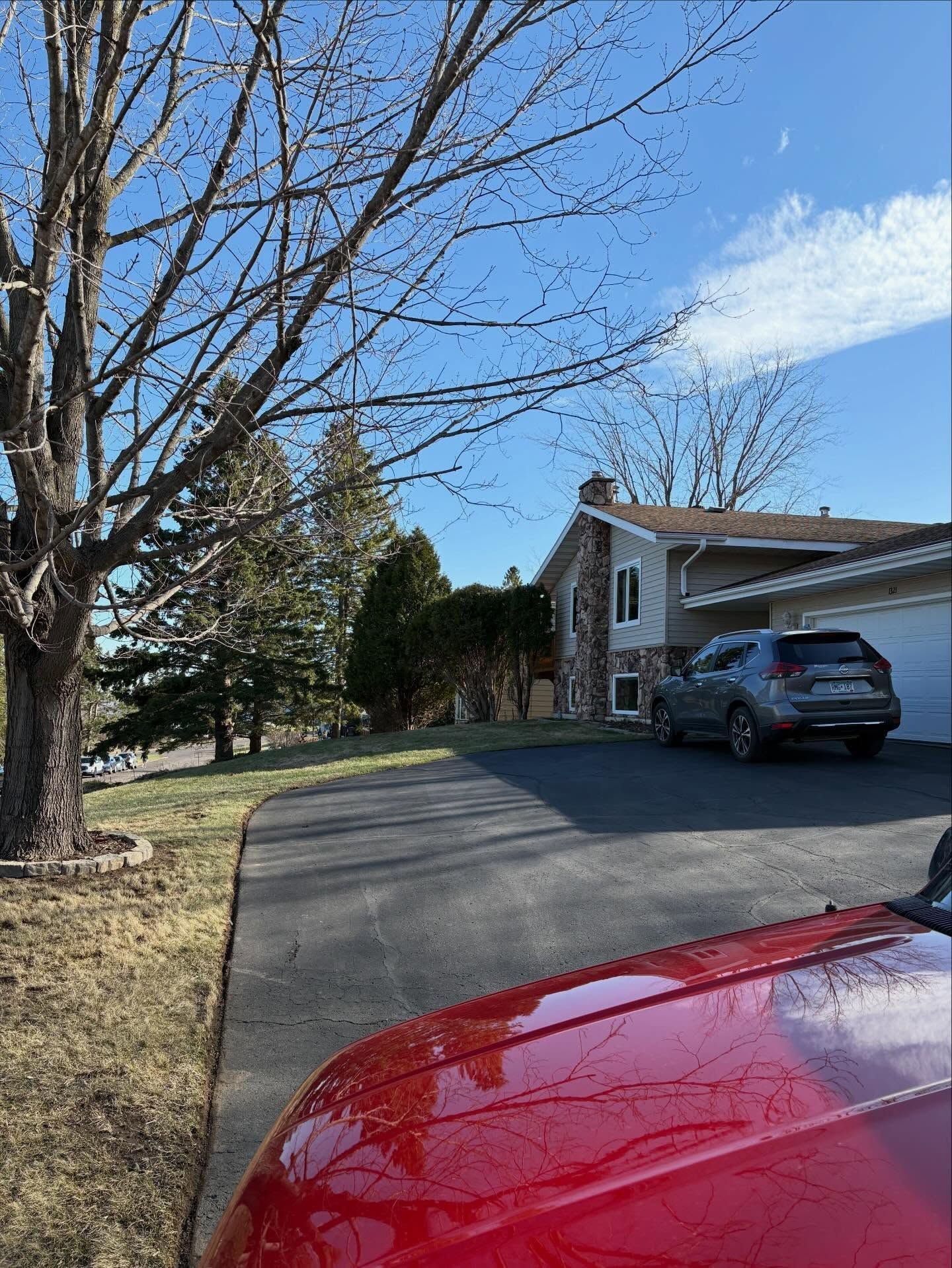 Driveway beside a house, with a red car in the foreground and a blue car parked near the garage.