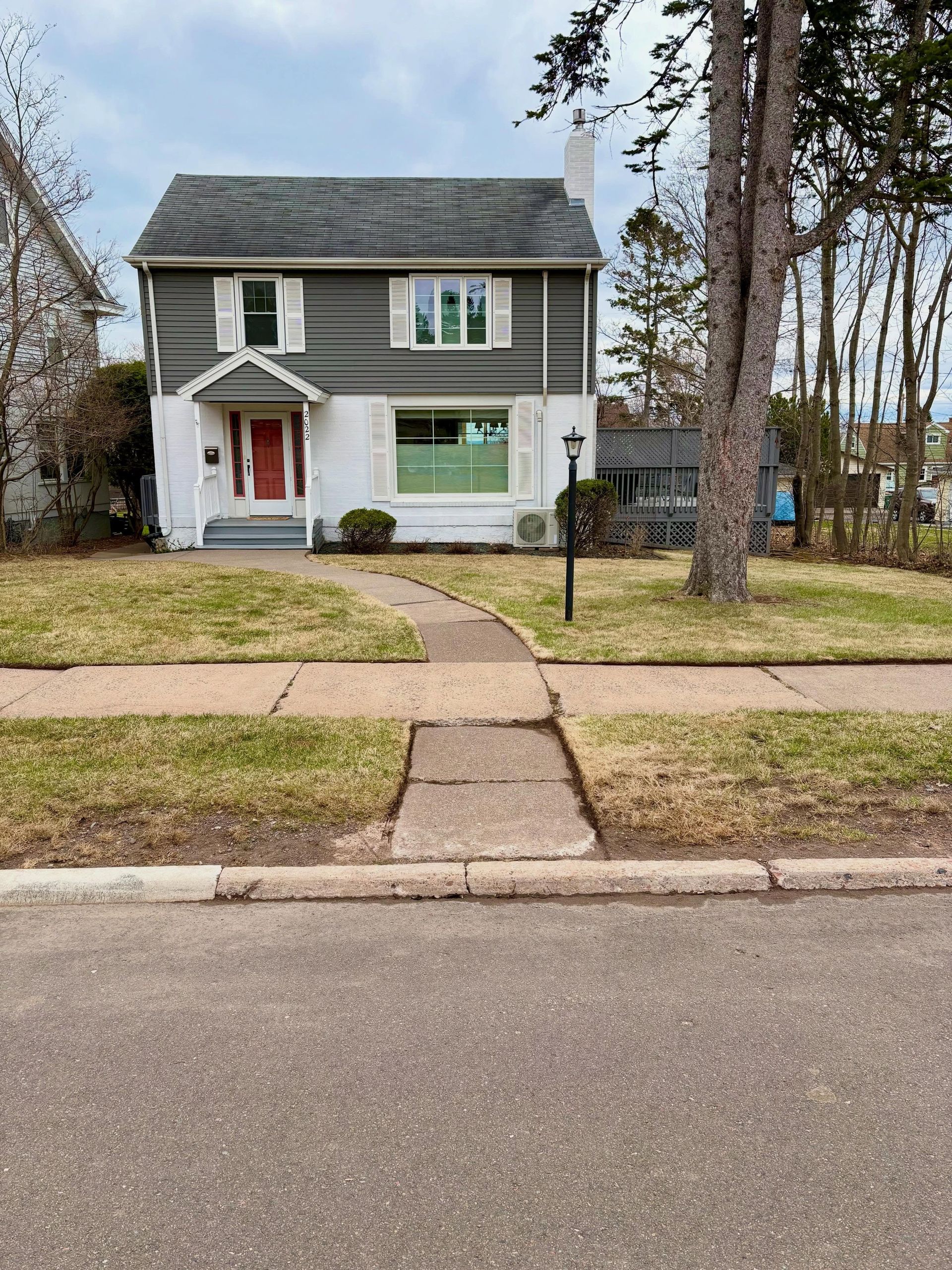 Two-story green house with red front door and a front walkway, seen from the street.