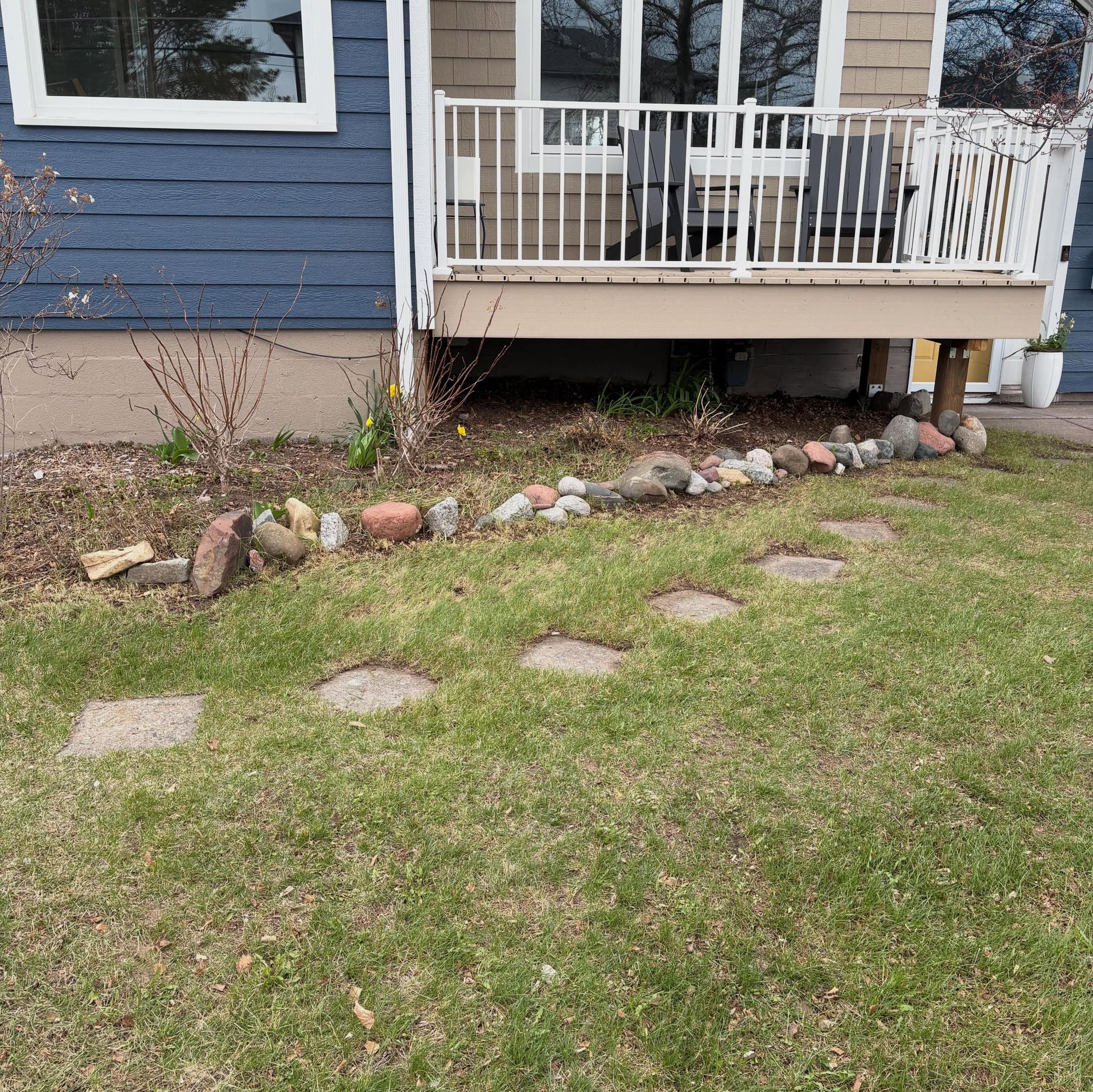 House porch with white railing, blue siding, and a rock border along a grassy yard