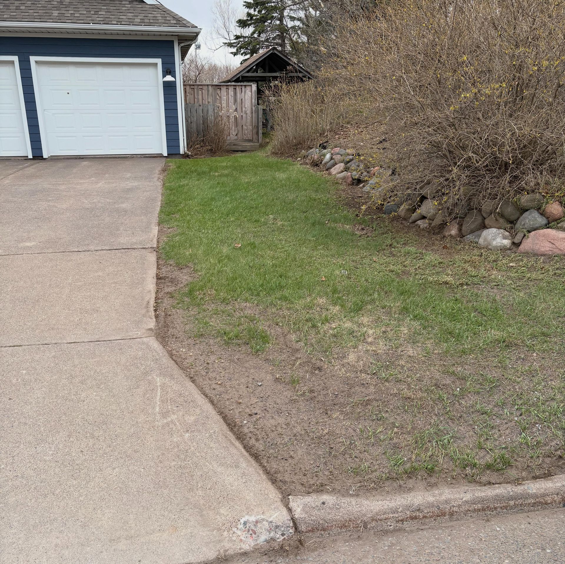 Driveway beside a garage, with a small grassy strip and shrubs along the edge.