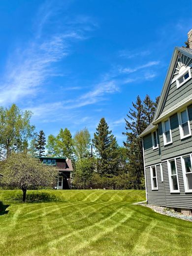 Gray house beside a sunny green lawn with trees and a blue sky