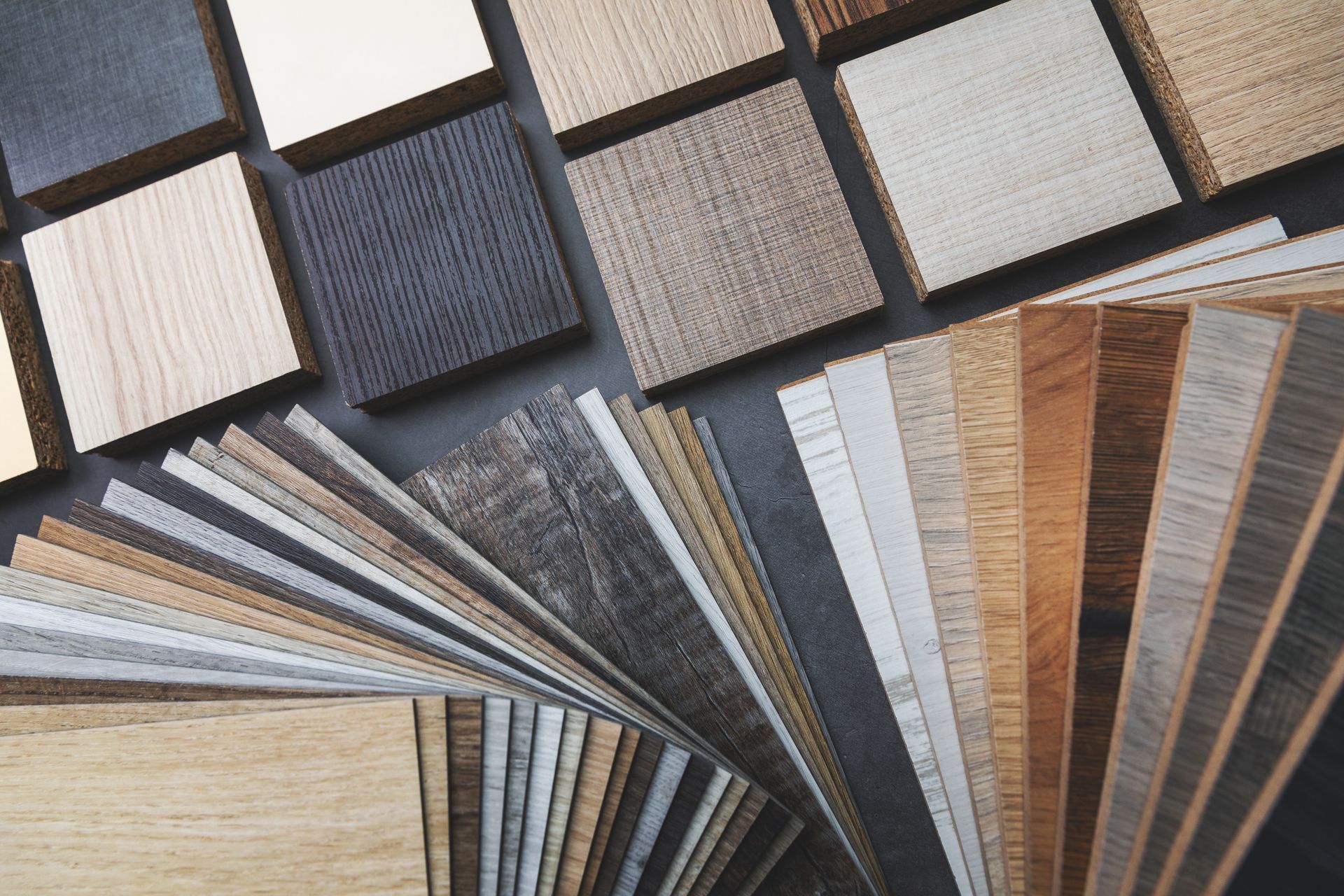 Wooden flooring samples in various colors and textures displayed on a dark surface.