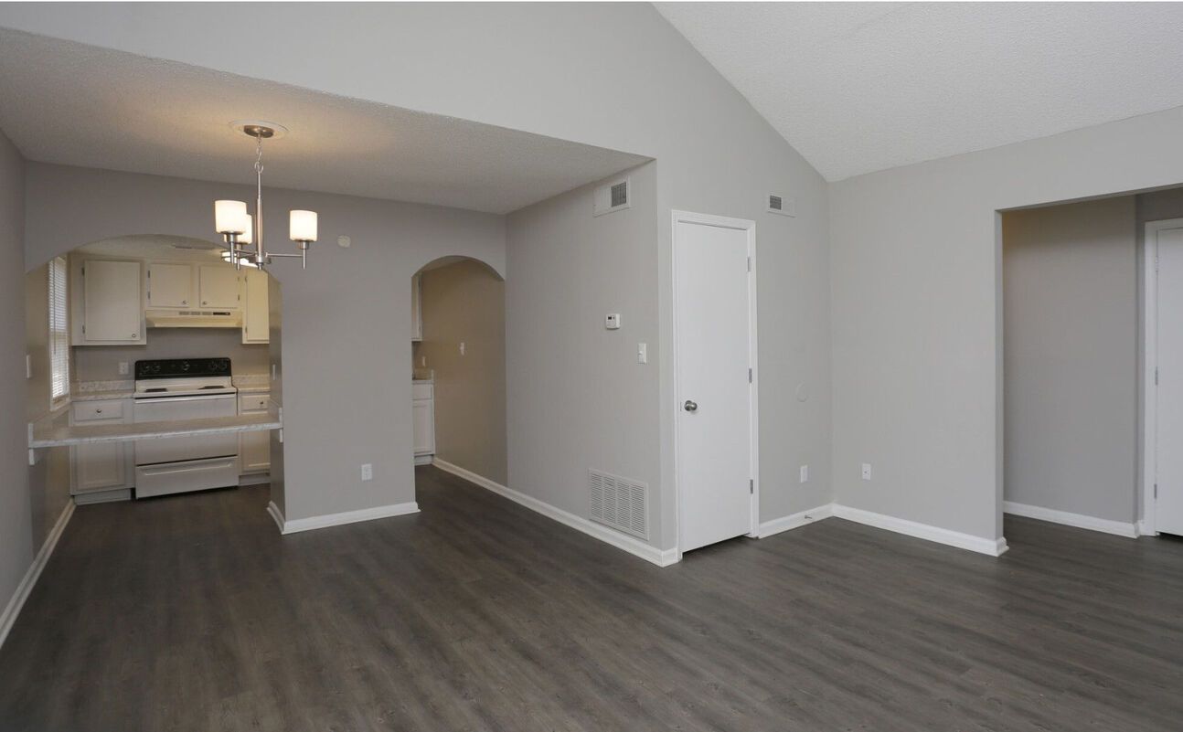 Interior of a living space with gray walls, dark wood-look flooring, and an entryway to a kitchen.