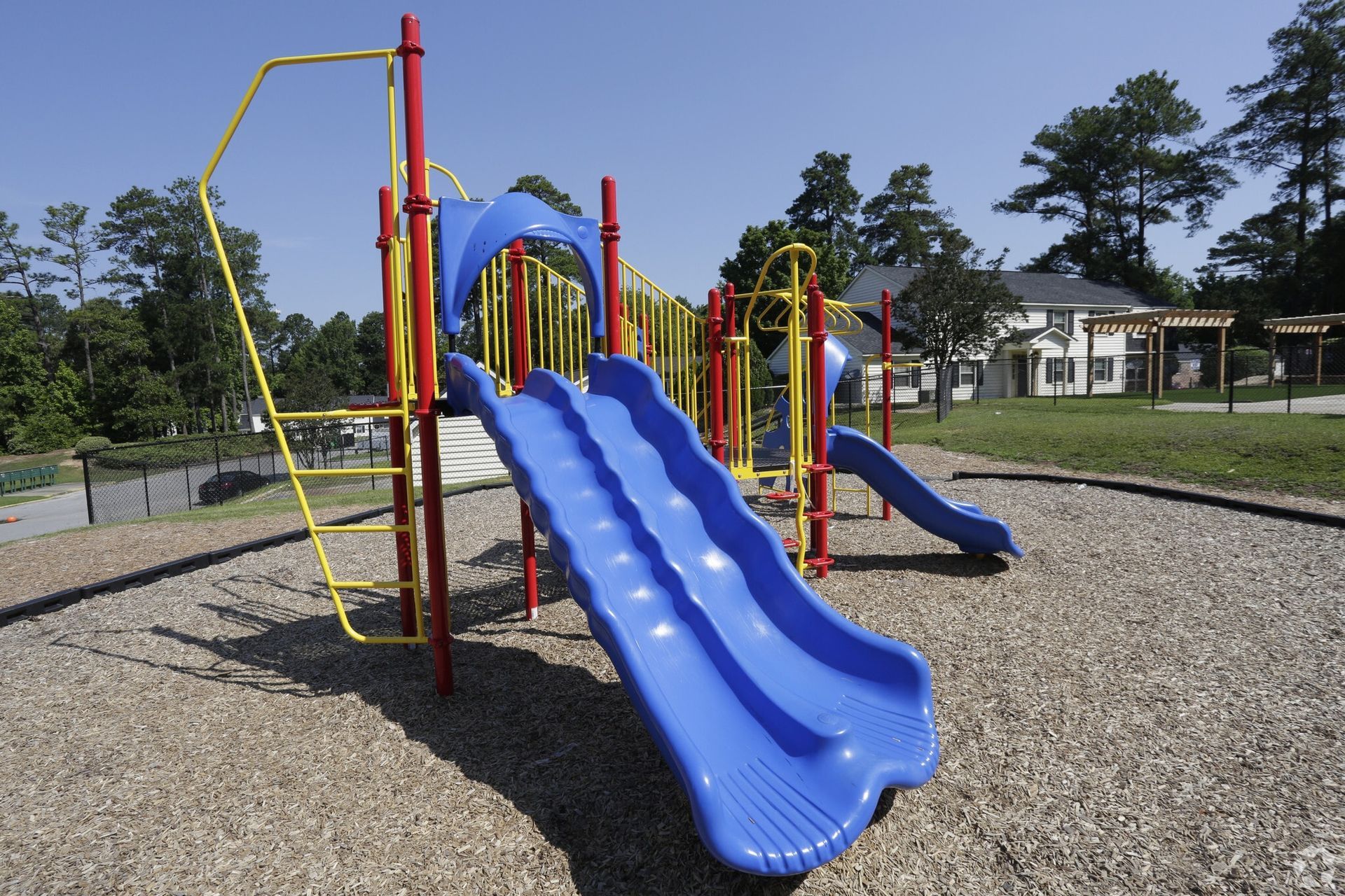 Playground with blue slide, red supports, yellow ladder, on wood-chip surface under blue sky.