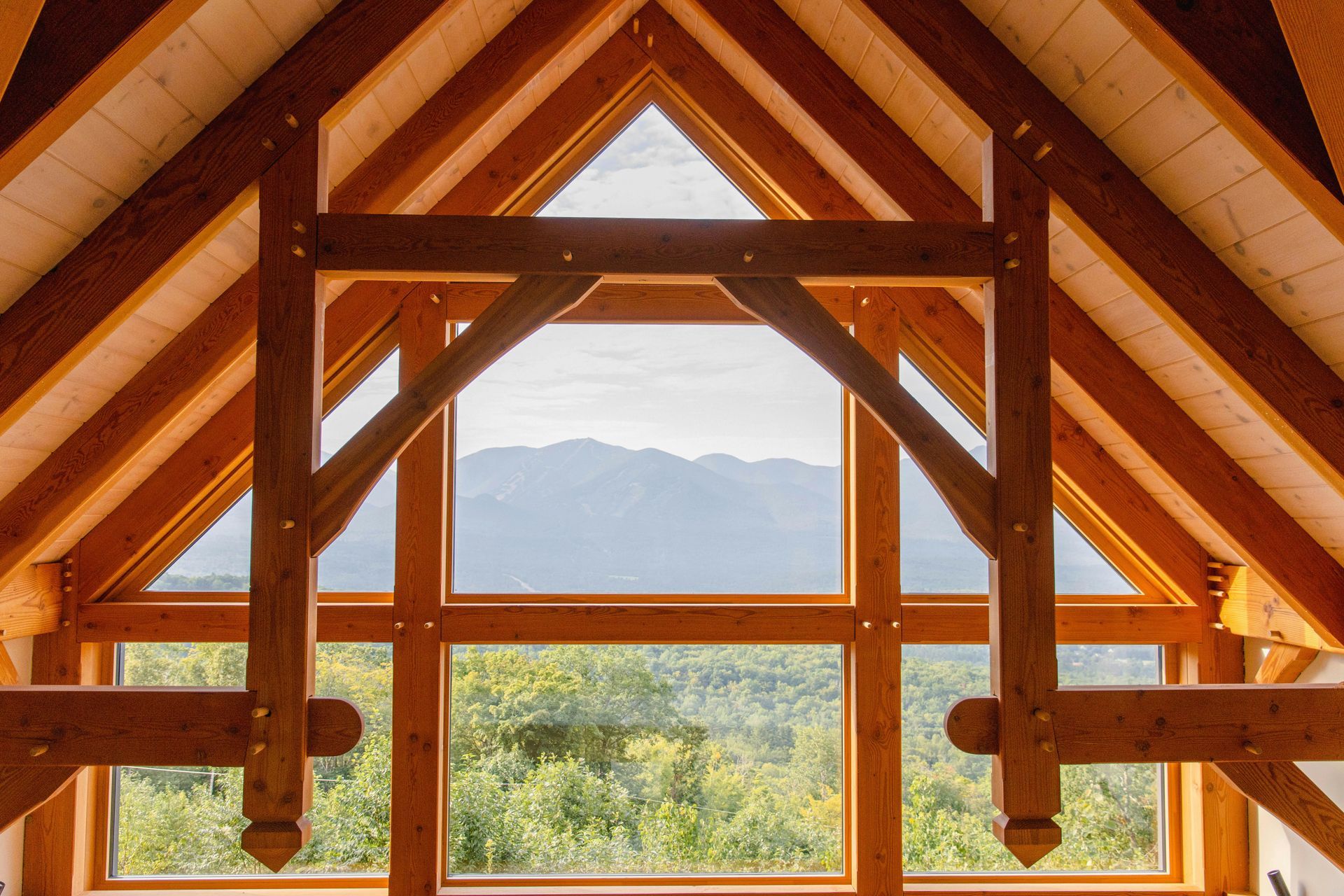 Wooden A-frame interior window framing mountains and green landscape outside
