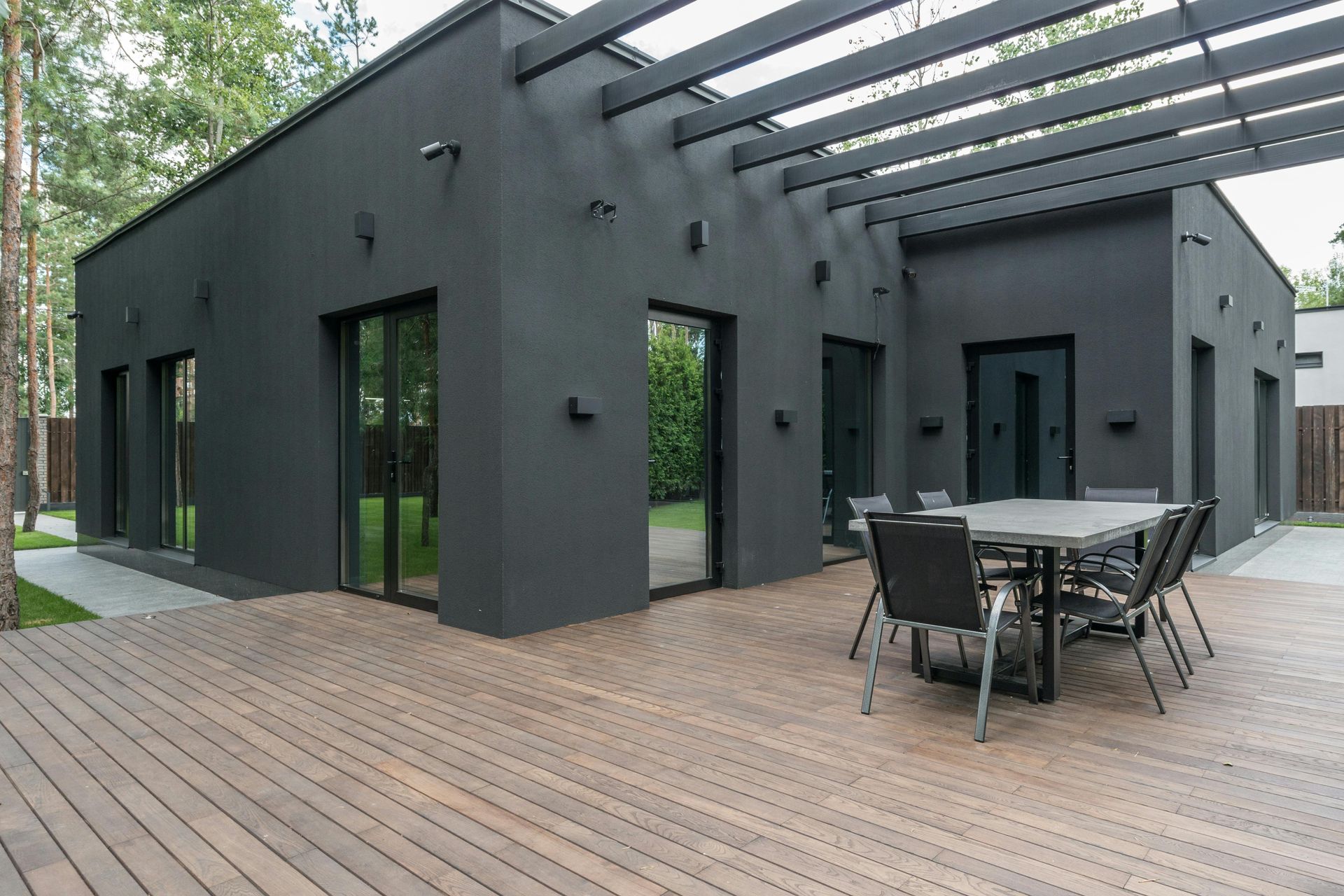 Modern black house with wooden deck and outdoor patio furniture under a pergola.