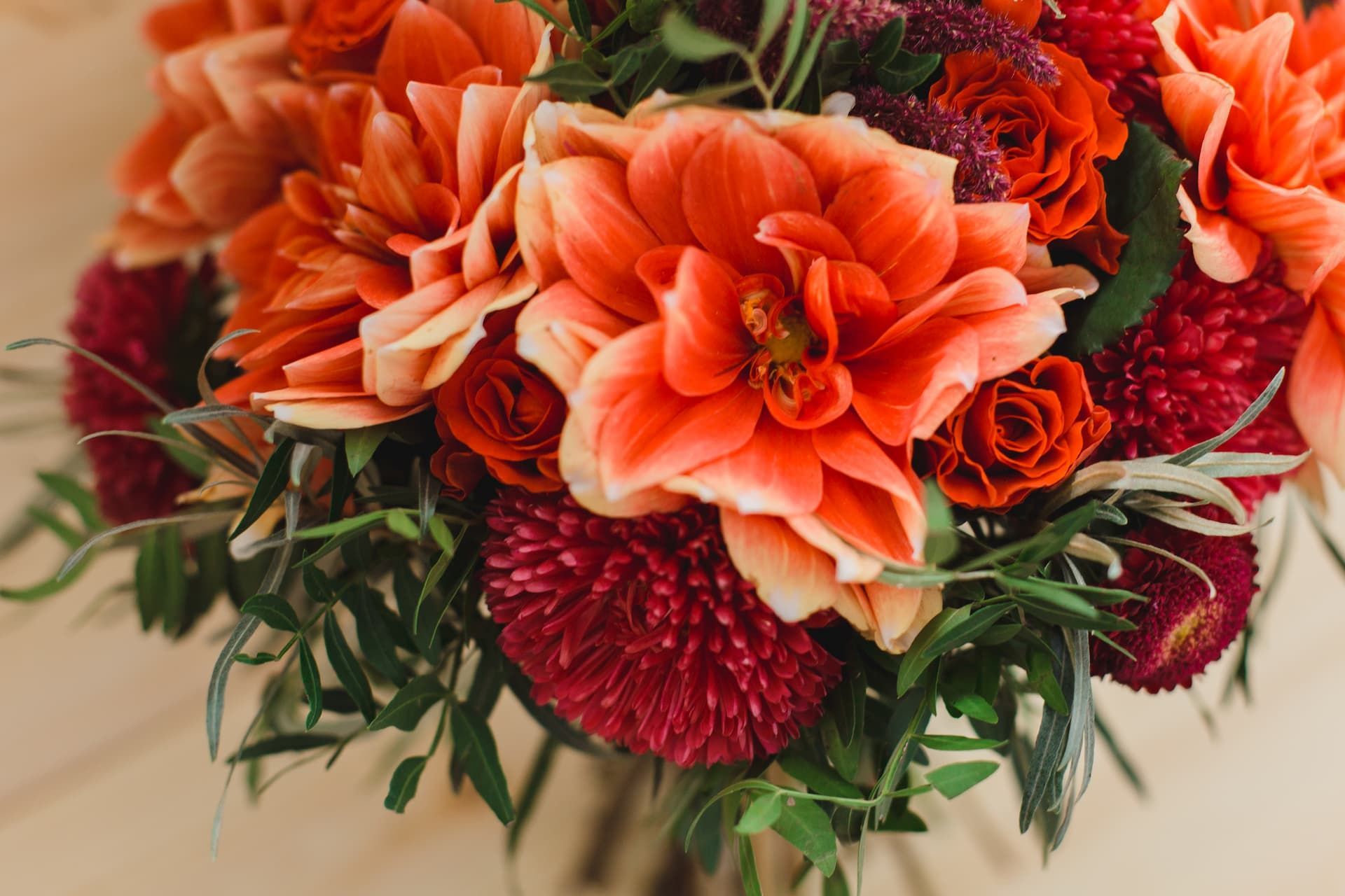 A close-up of a bouquet featuring vibrant orange dahlias, deep red chrysanthemums, and small greenery.