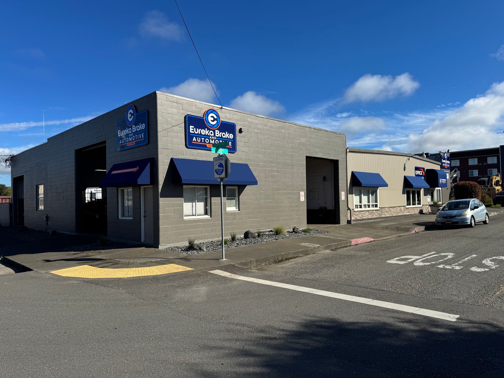 A gray brick commercial building with blue awnings, signs reading