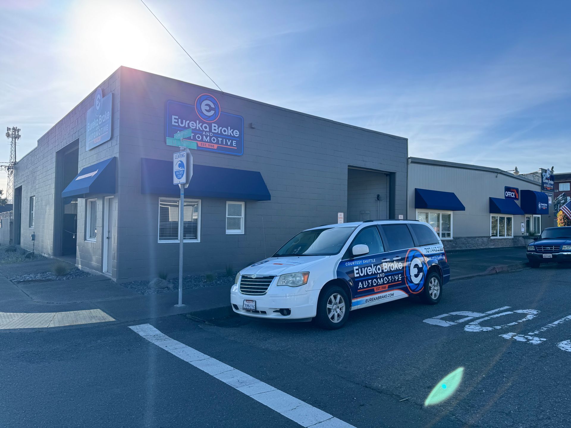 Gray building with blue sign and awning, with a white-and-blue service van parked outside in sunlight | Eureka Brake & Automotive