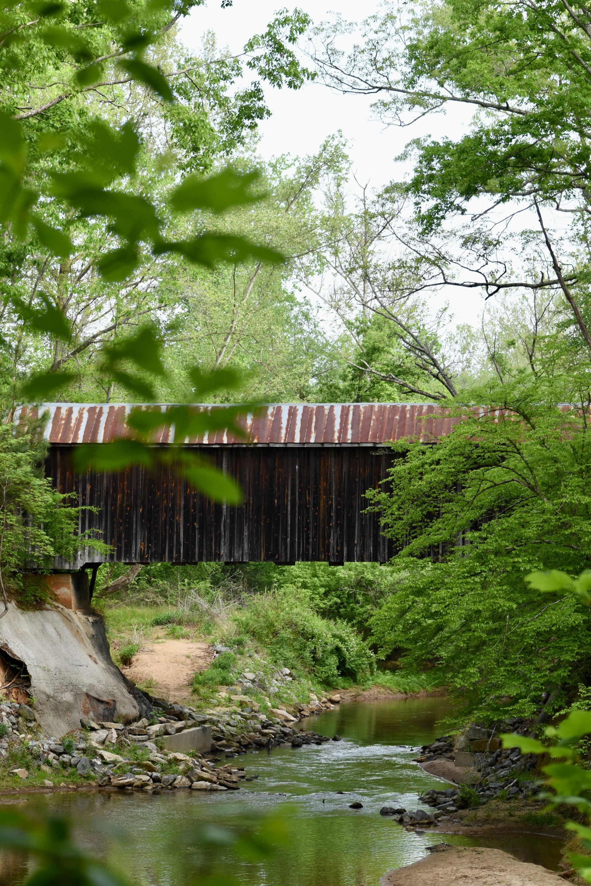 Wooden covered bridge over a creek, surrounded by green trees.